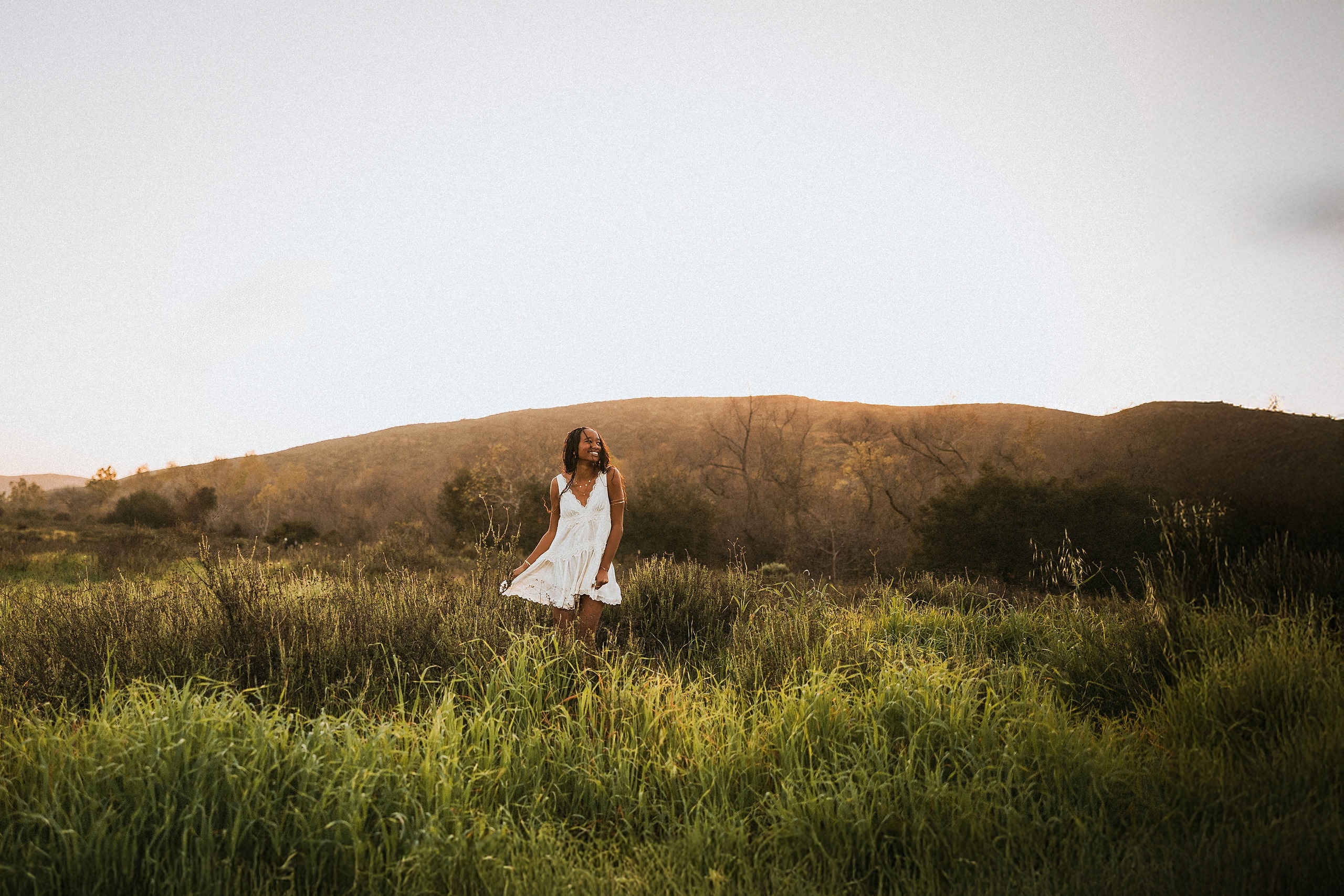 San Diego Senior Photos — 20 Kaelyn in white dress walking through grassy area near Steele Canyon with hills