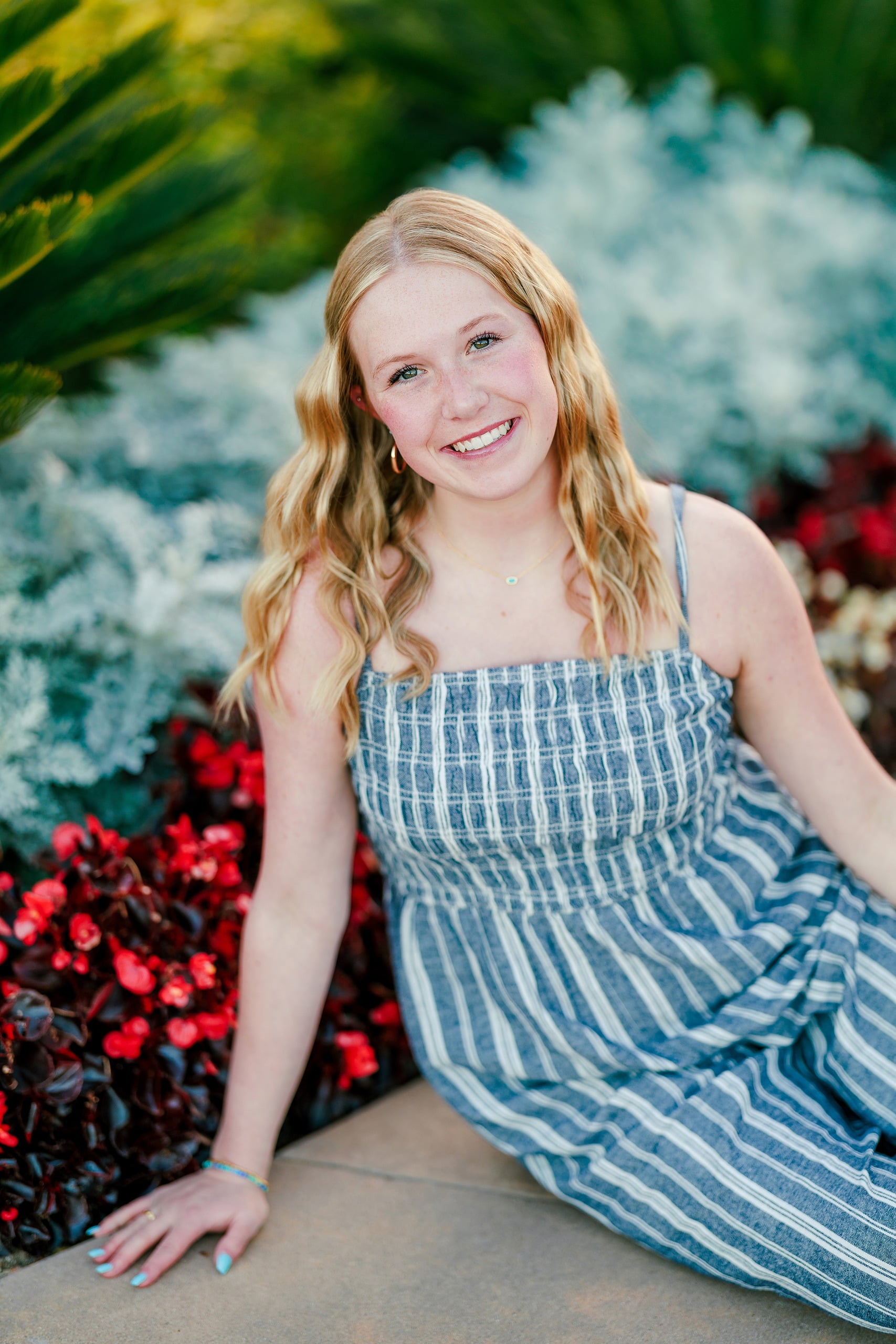 Sisters & Senior Portraits at the Del — 04 Teen sitting in sand surrounded by red and white flowers at the Del