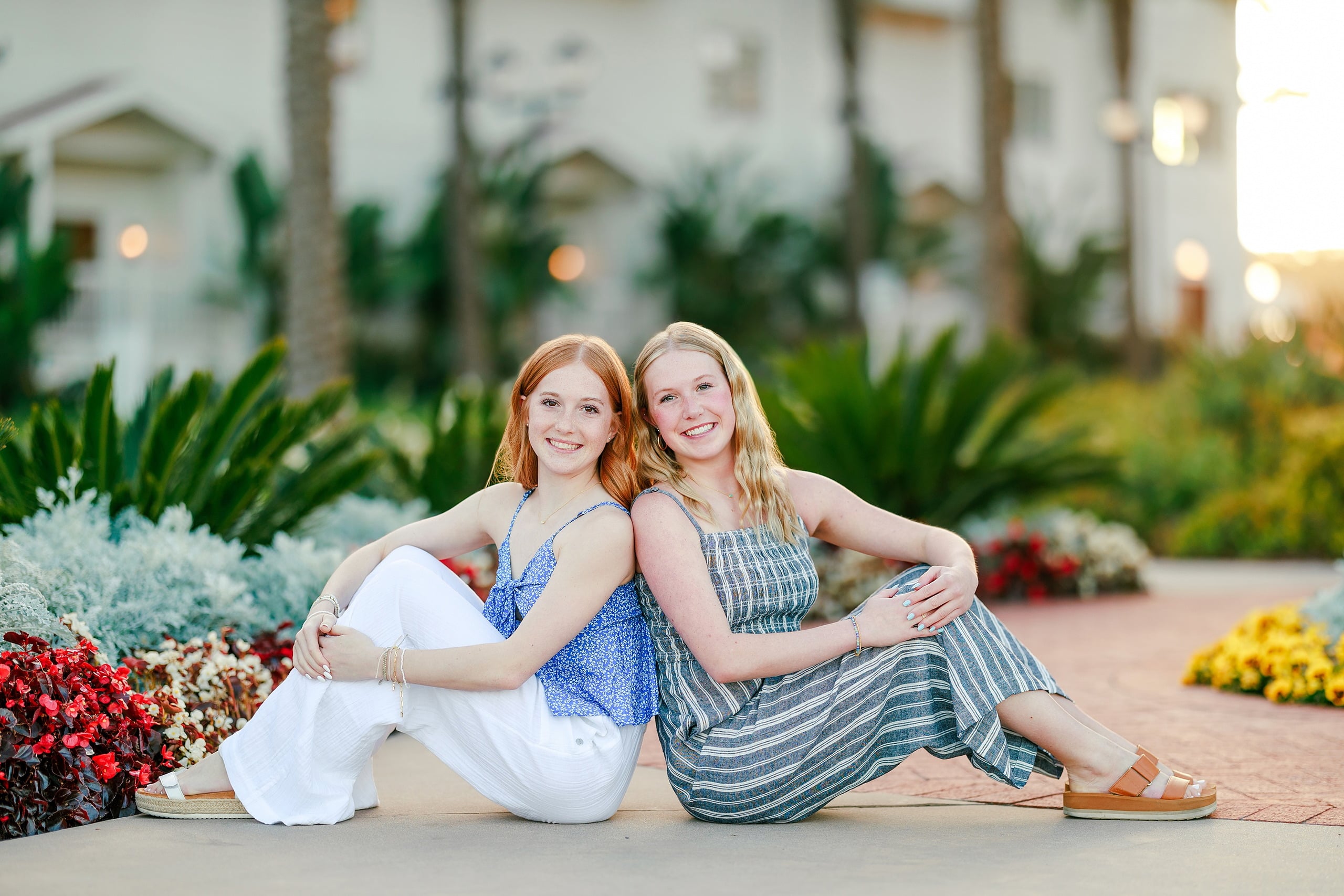 Sisters & Senior Portraits at the Del — 08 Two teens sitting in sand among red flowers and blue-green foliage