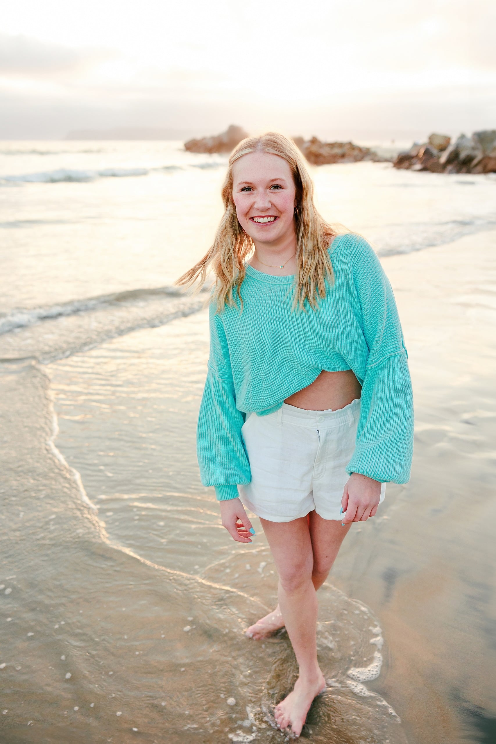 Sisters & Senior Portraits at the Del — 21 Teen wading in shallow water wearing turquoise sweater and white shorts