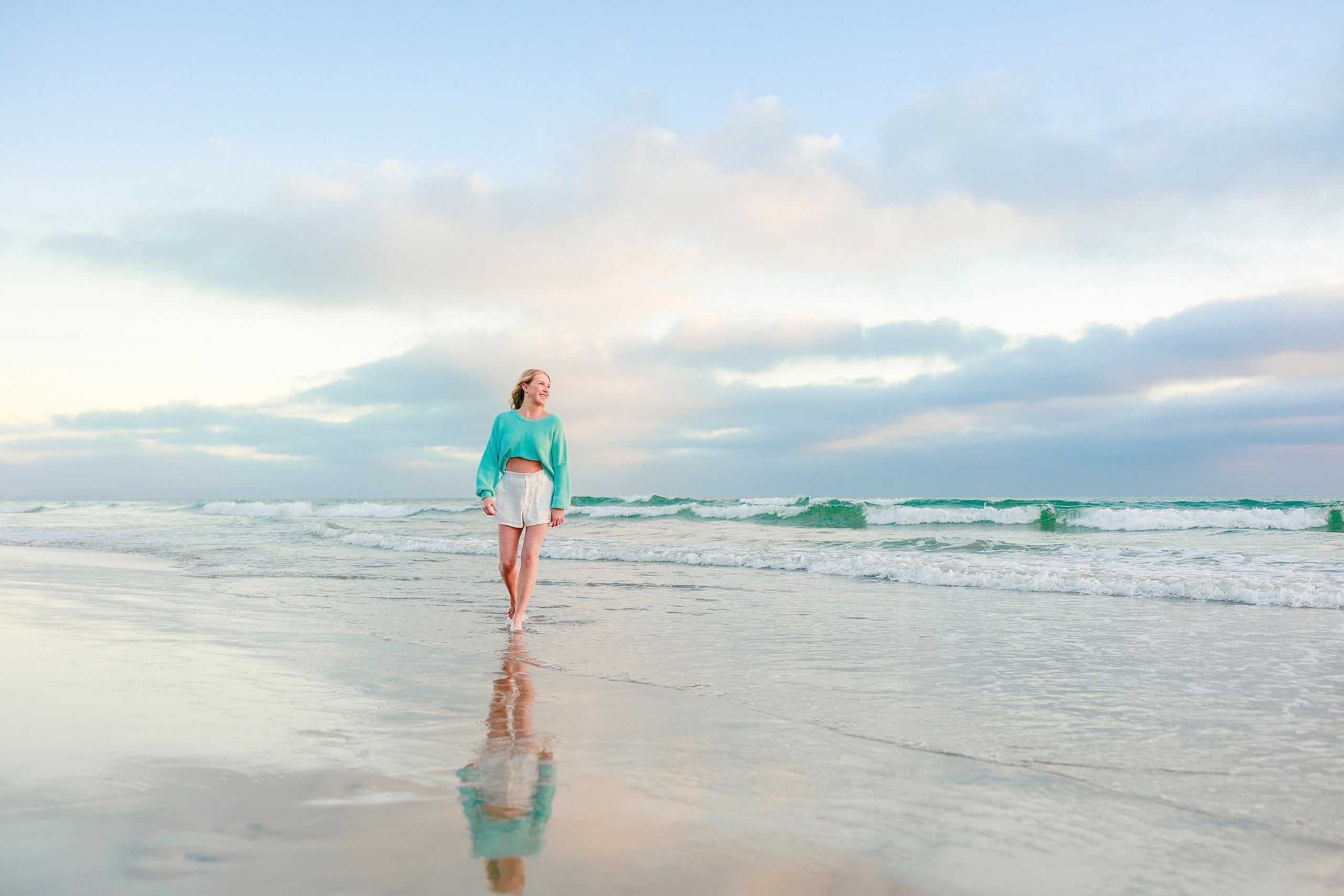 Sisters & Senior Portraits at the Del — 22 Teen in turquoise sweater and white shorts walking through wet beach sand