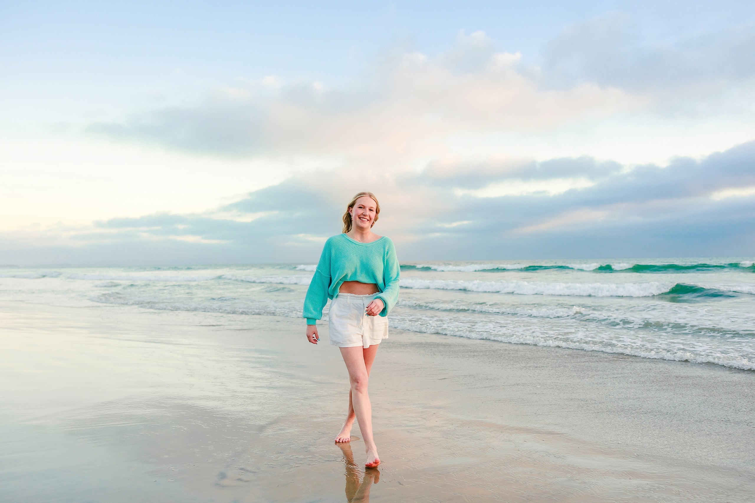 Sisters & Senior Portraits at the Del — 23 Teen near large rocky formations on beach wearing turquoise sweater