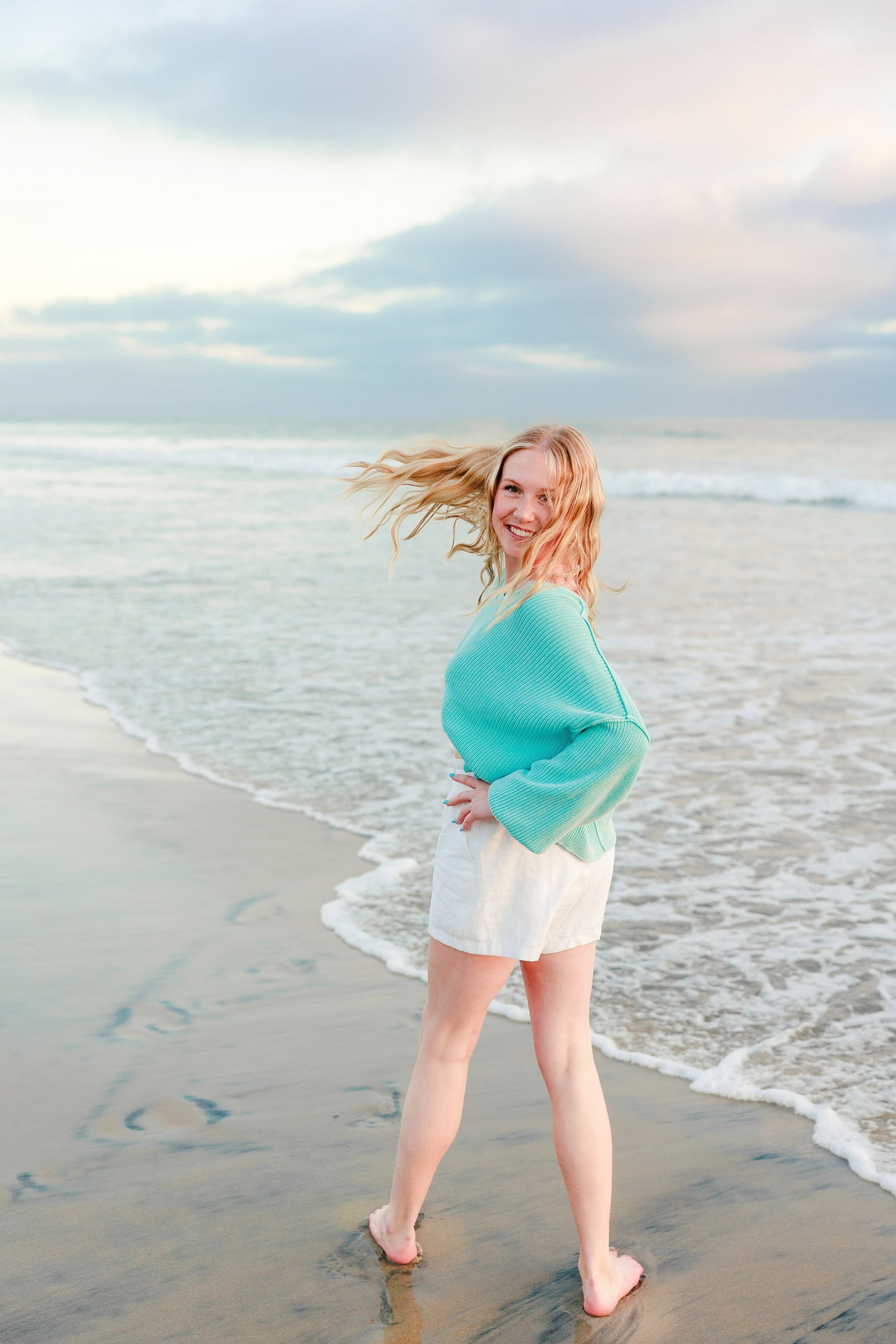 Sisters & Senior Portraits at the Del — 25 Teen in blue floral top and white linen pants standing on sandy beach