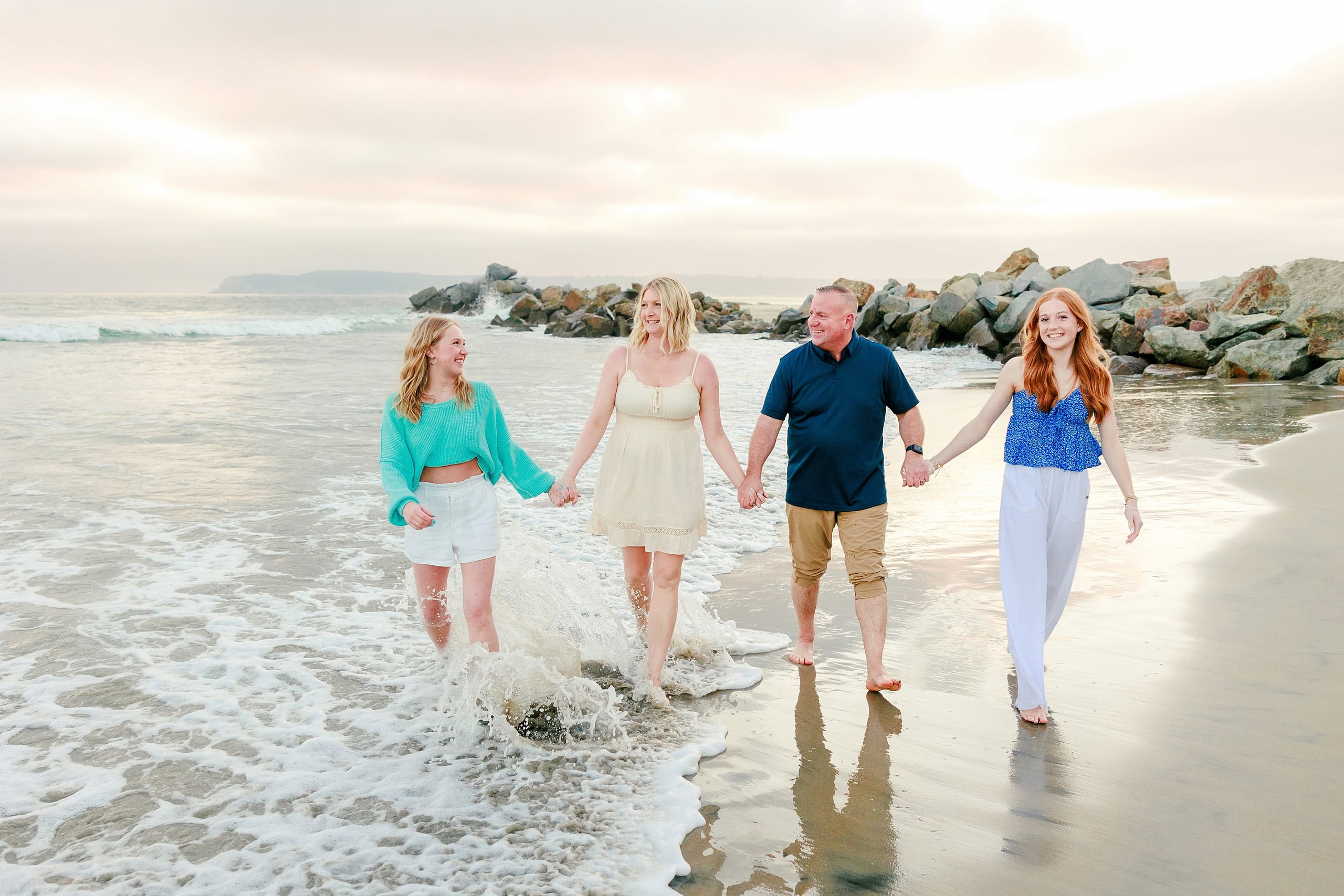 Sisters & Senior Portraits at the Del — 31 Two sisters hugging on beach with rocky jetty and waves in background