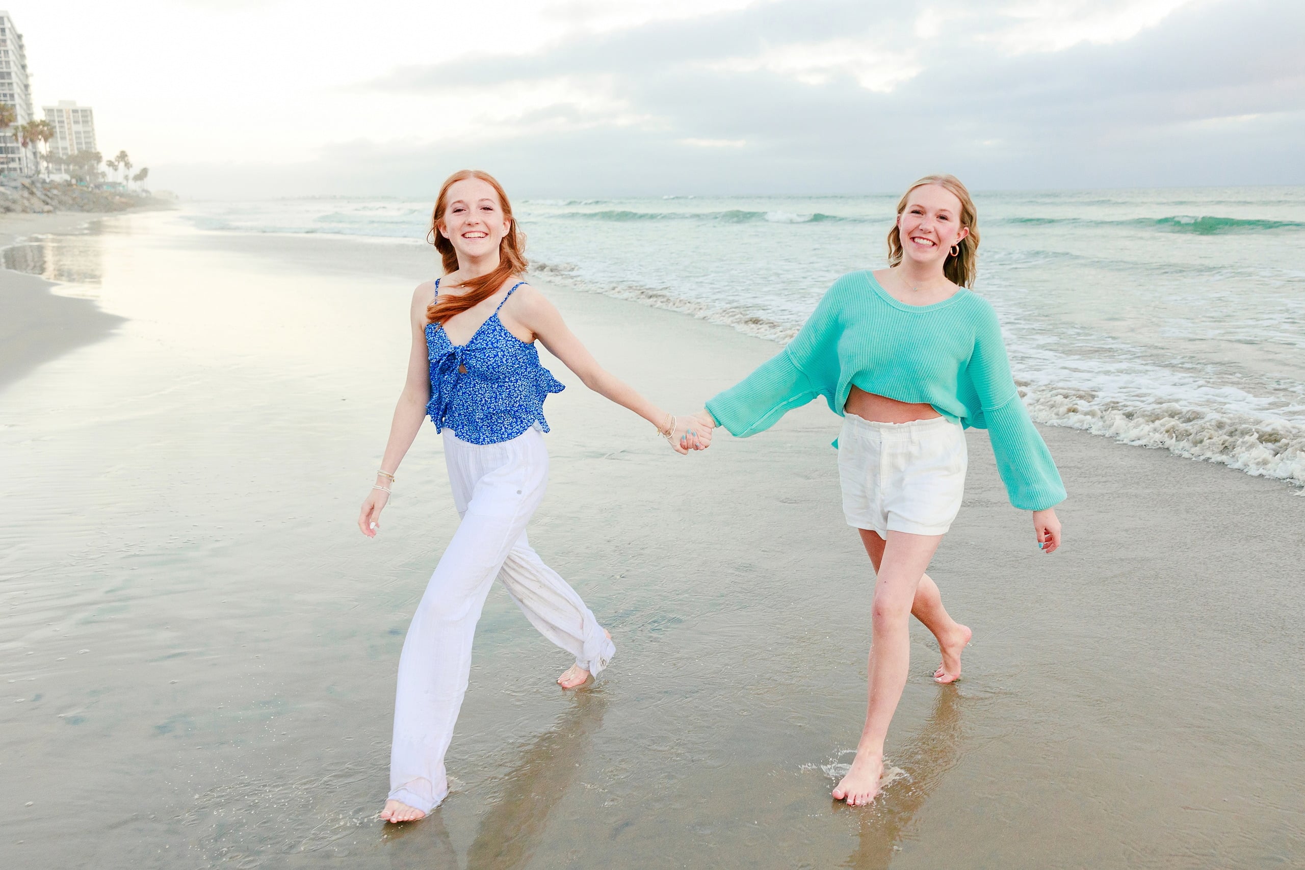 Sisters & Senior Portraits at the Del — 32 Two sisters embracing on beach with Hotel del Coronado's tower visible behind