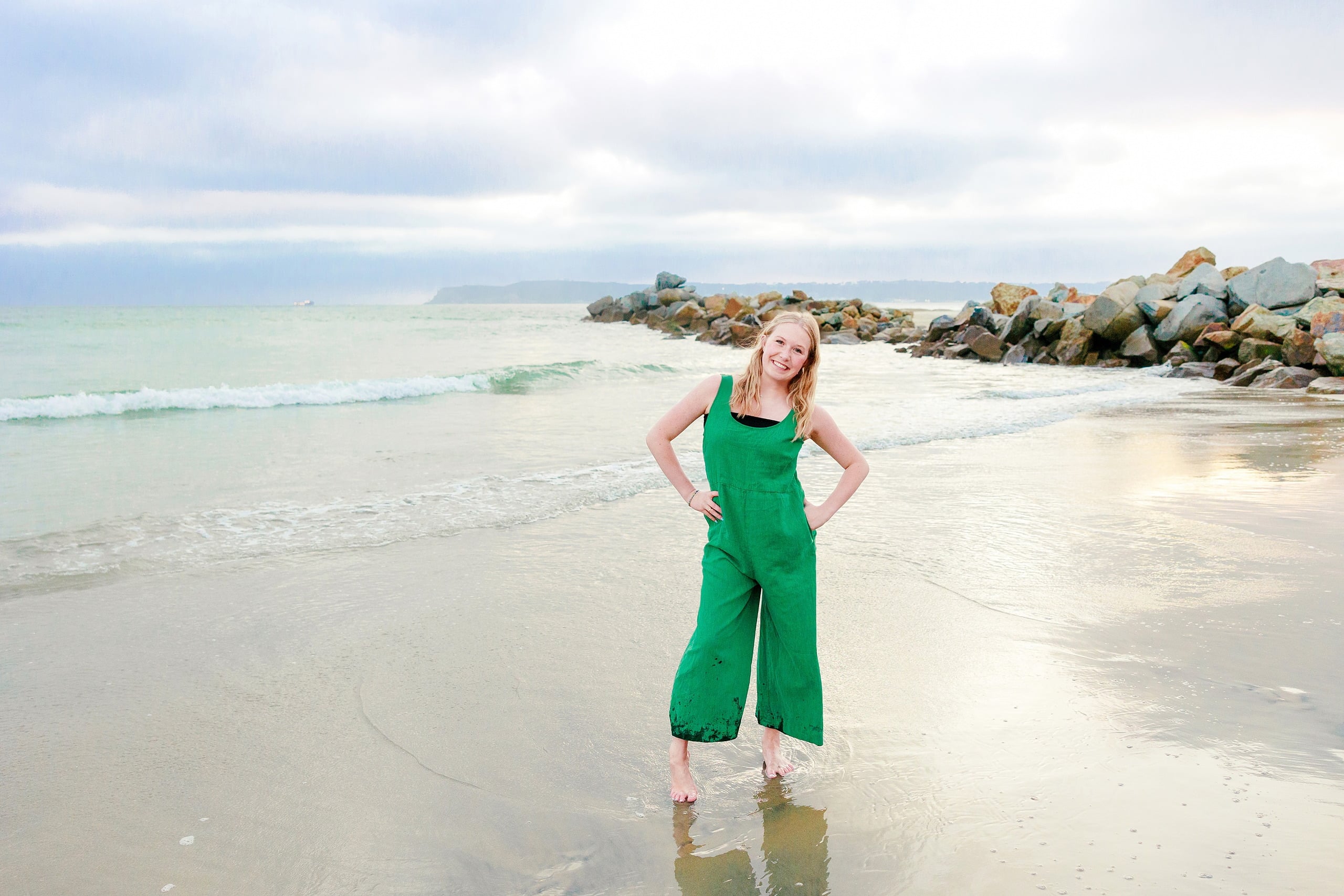 Sisters & Senior Portraits at the Del — 37 Teen in green romper resting one hand against large, weathered beach boulder