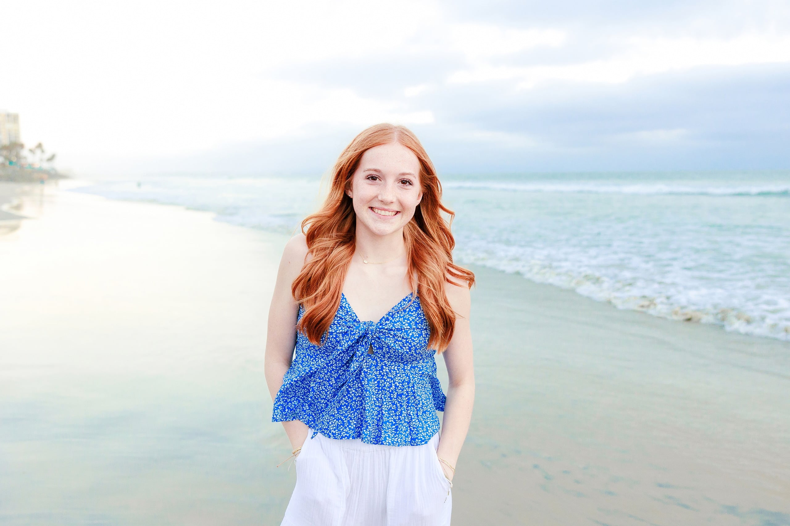 Sisters & Senior Portraits at the Del — 40 Two sisters sitting on sand with Hotel del Coronado's red-roofed building visible