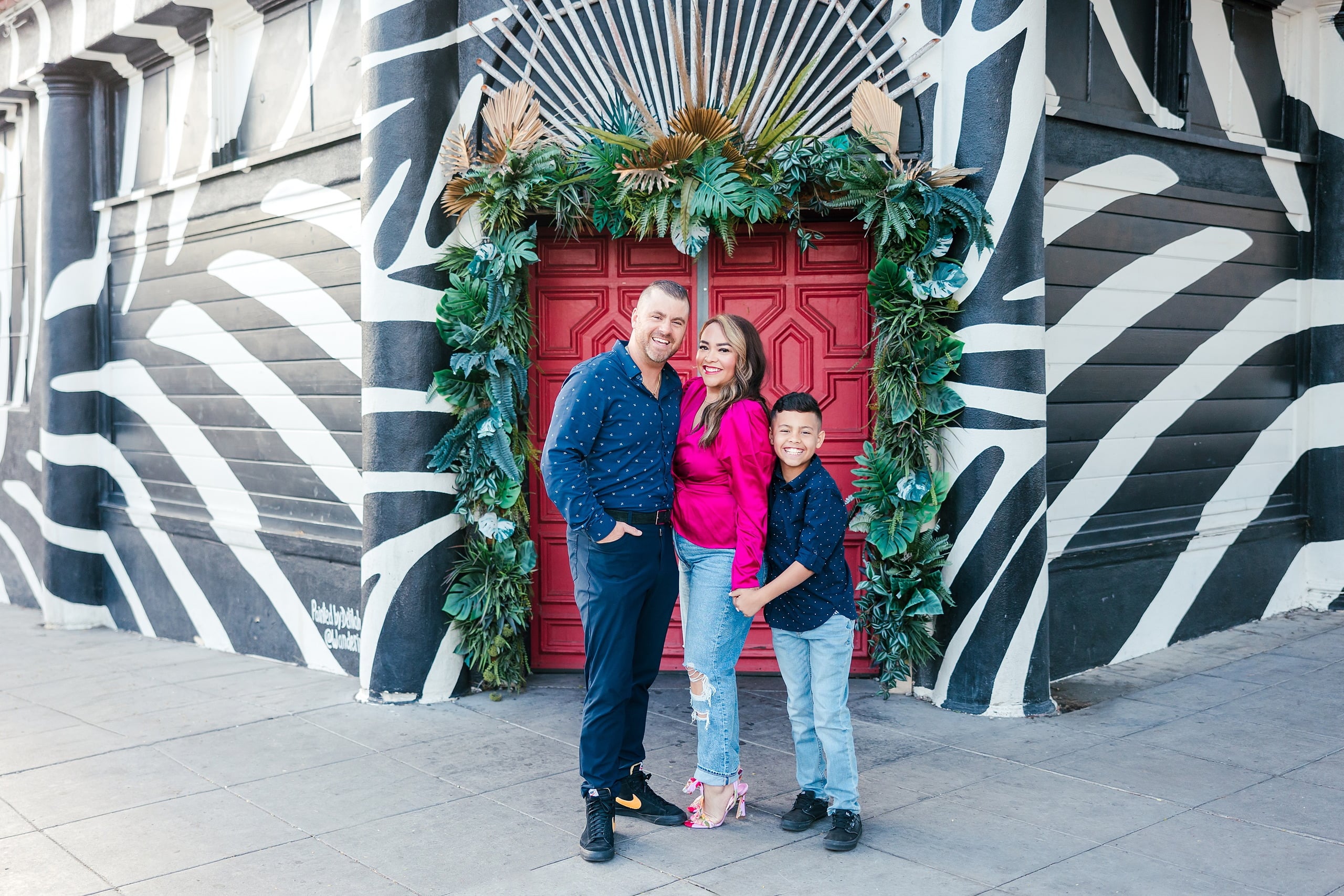 Spring Break Surprise: Why This Mom Booked a Secret Photo Session — 01 Man, woman, and child standing before red door with garland in Little Italy