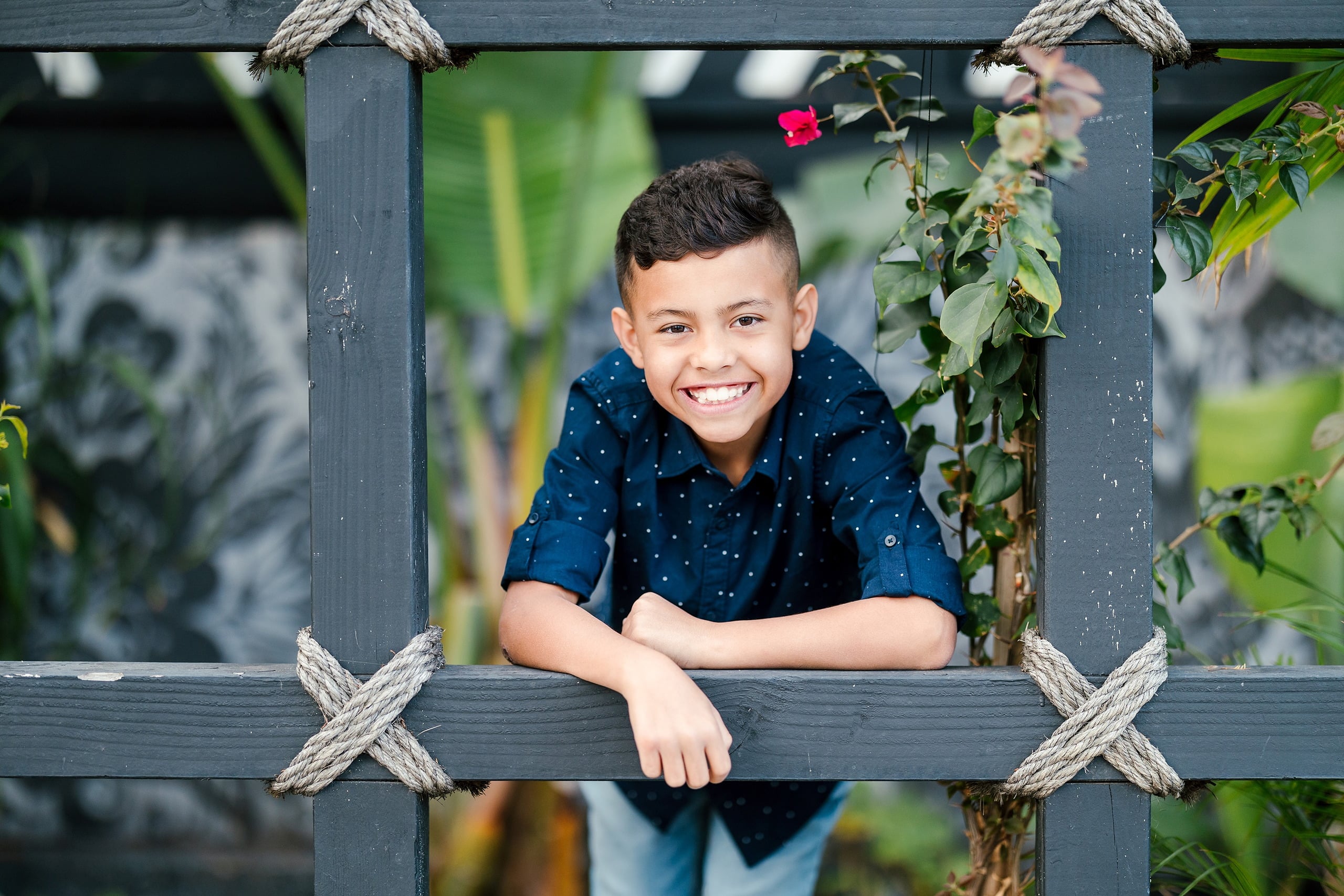 Spring Break Surprise: Why This Mom Booked a Secret Photo Session — 04 Child smiles through ornate black trellis in garden, Little Italy