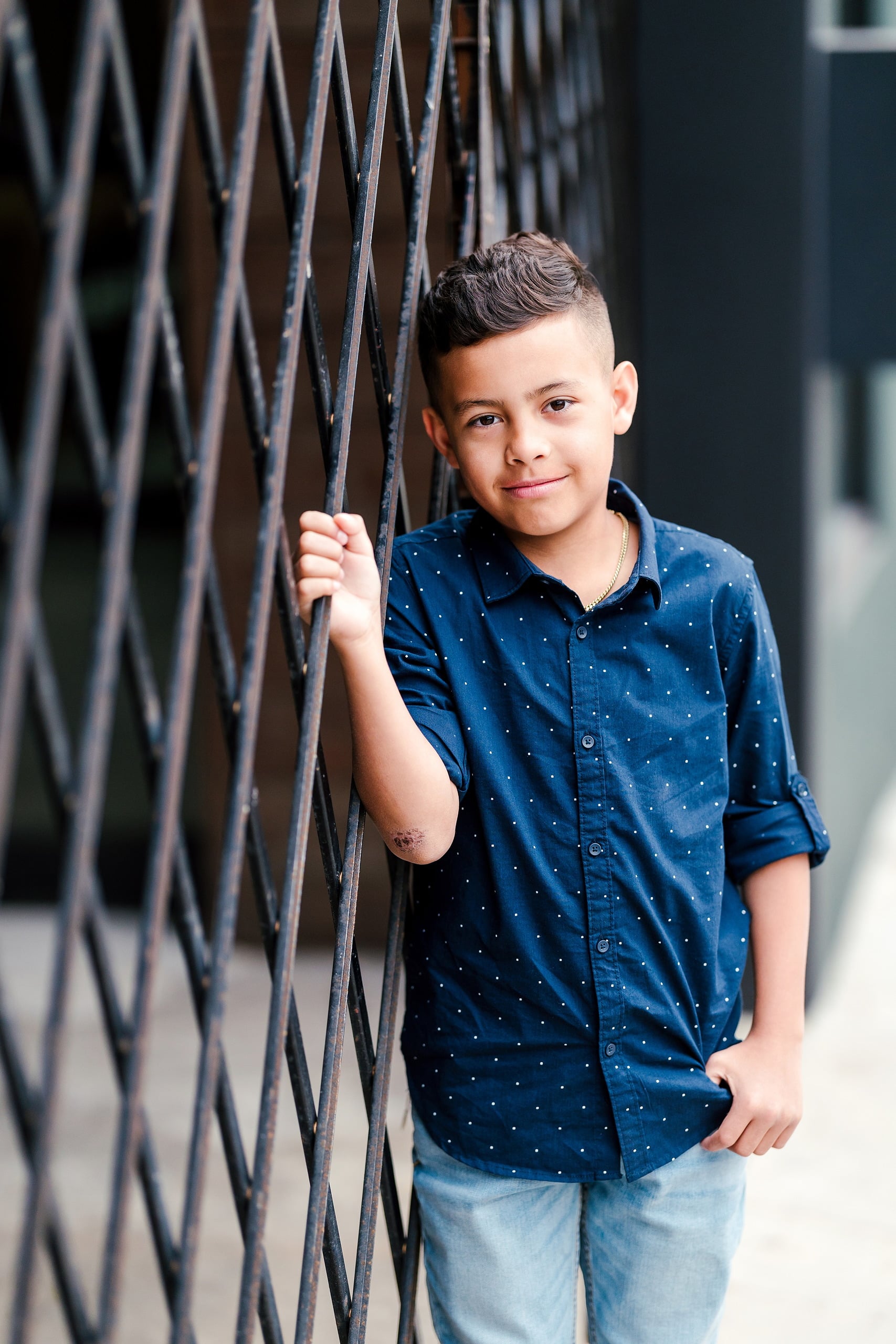 Spring Break Surprise: Why This Mom Booked a Secret Photo Session — 05 Child poses with hand on chain-link fence against urban street