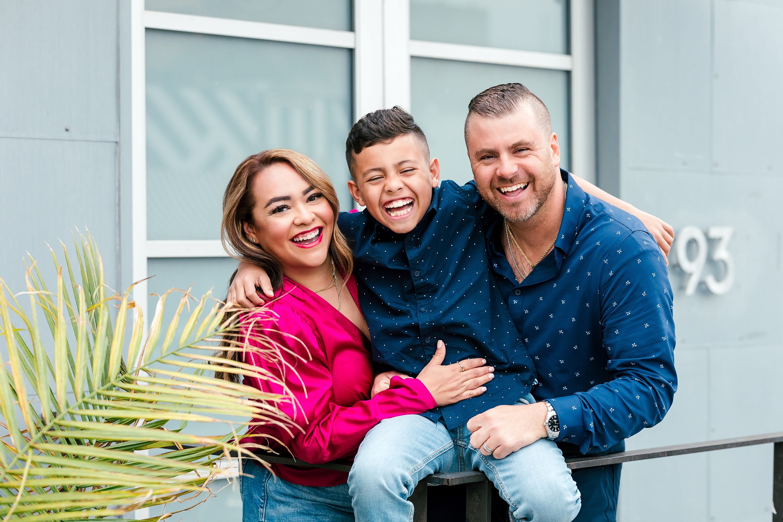 Spring Break Surprise: Why This Mom Booked a Secret Photo Session — 11 Man, woman, and child laugh together on railing with palm plants