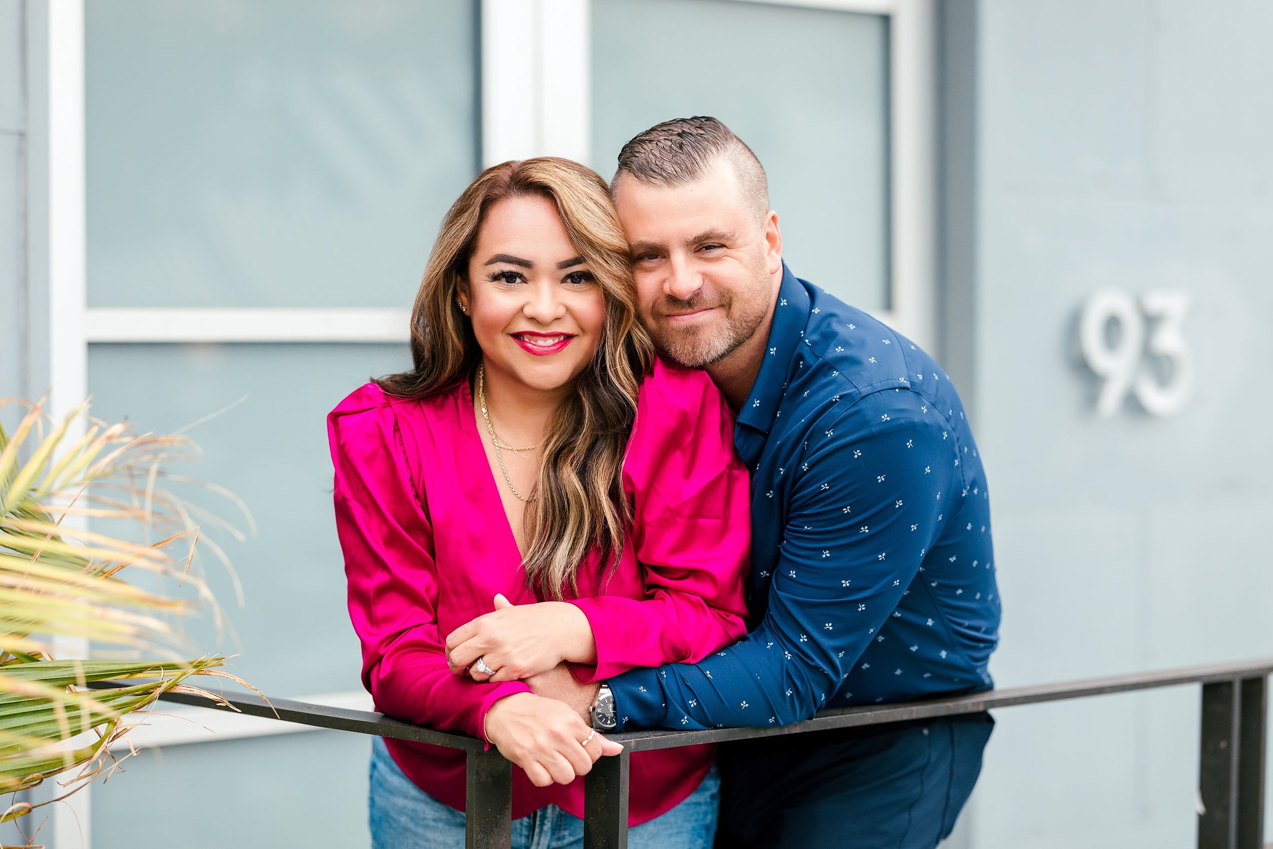 Spring Break Surprise: Why This Mom Booked a Secret Photo Session — 12 Woman in hot pink sits on railing with palm plant, urban backdrop