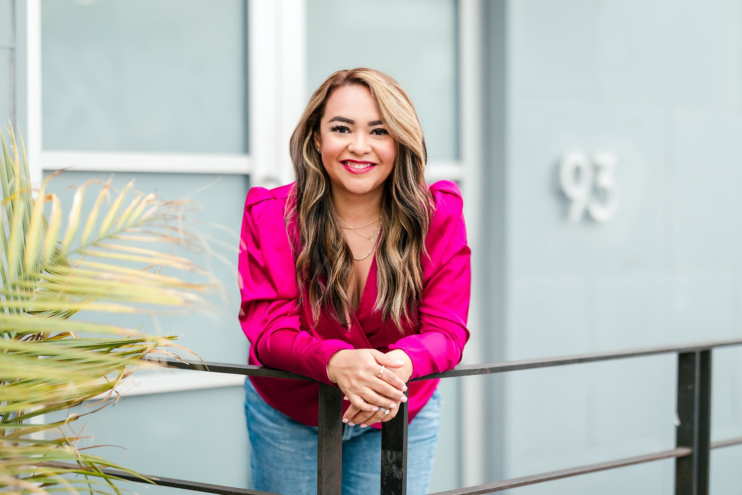 Spring Break Surprise: Why This Mom Booked a Secret Photo Session — 13 Man leans on railing with palm plant, modern glass building behind