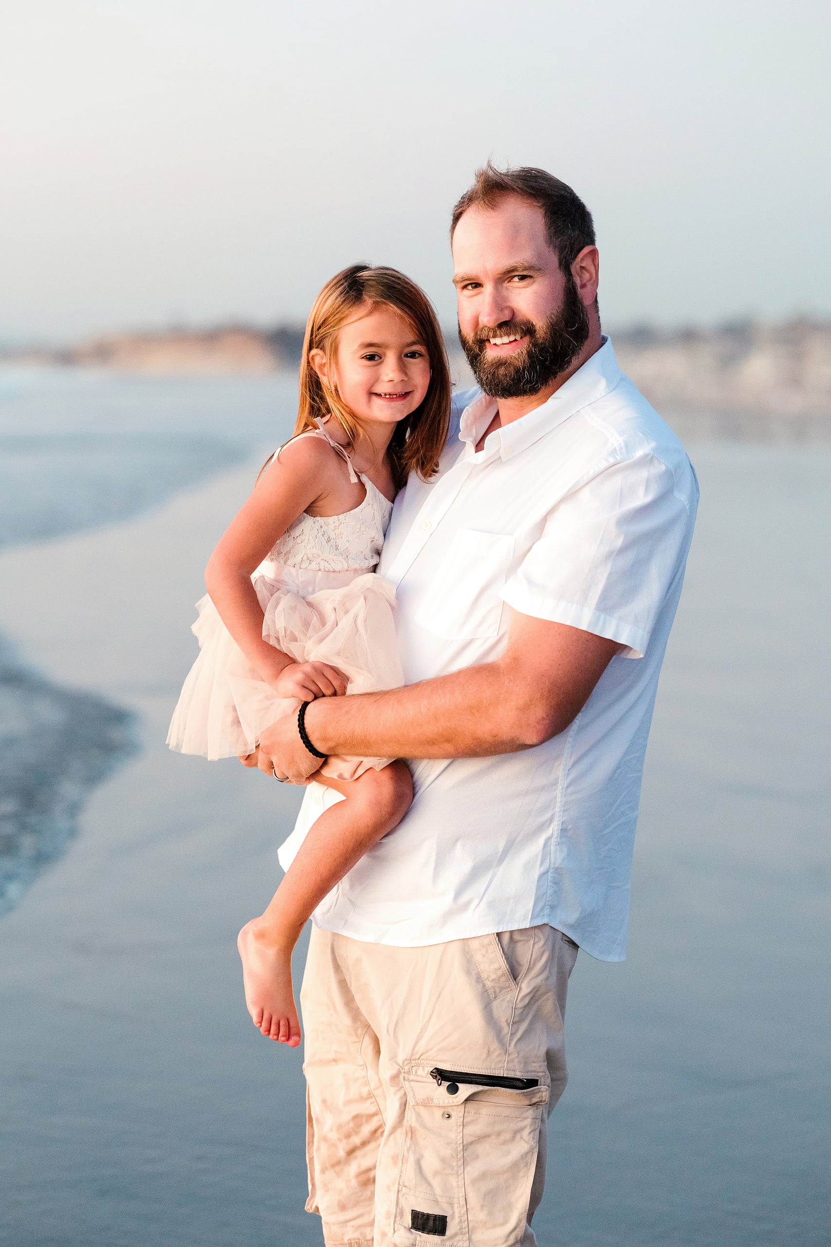 The Day the Sun Stood Still — 04 Man holding young girl in white dress standing on wet beach sand at Del Mar