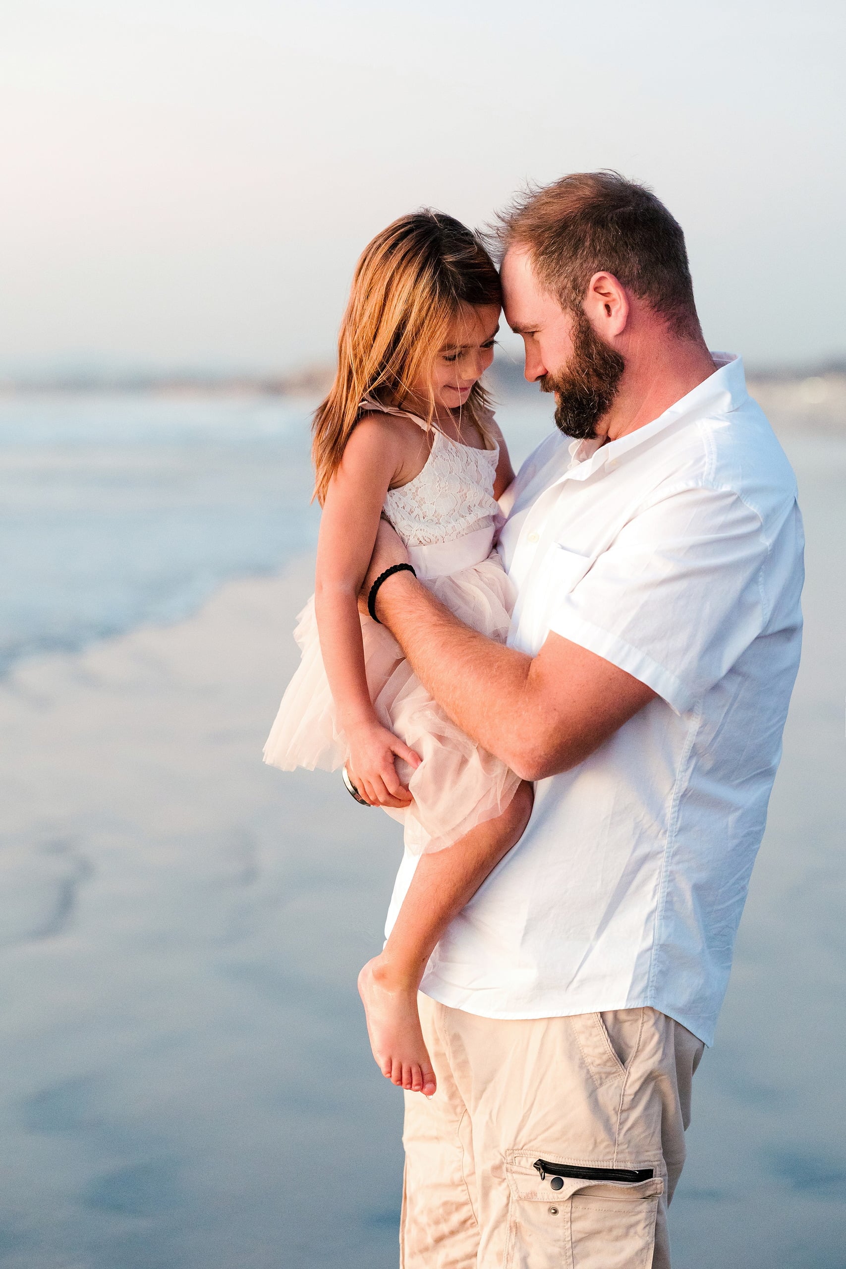 The Day the Sun Stood Still — 09 Man holding young child in pale pink dress on wet beach sand at Del Mar