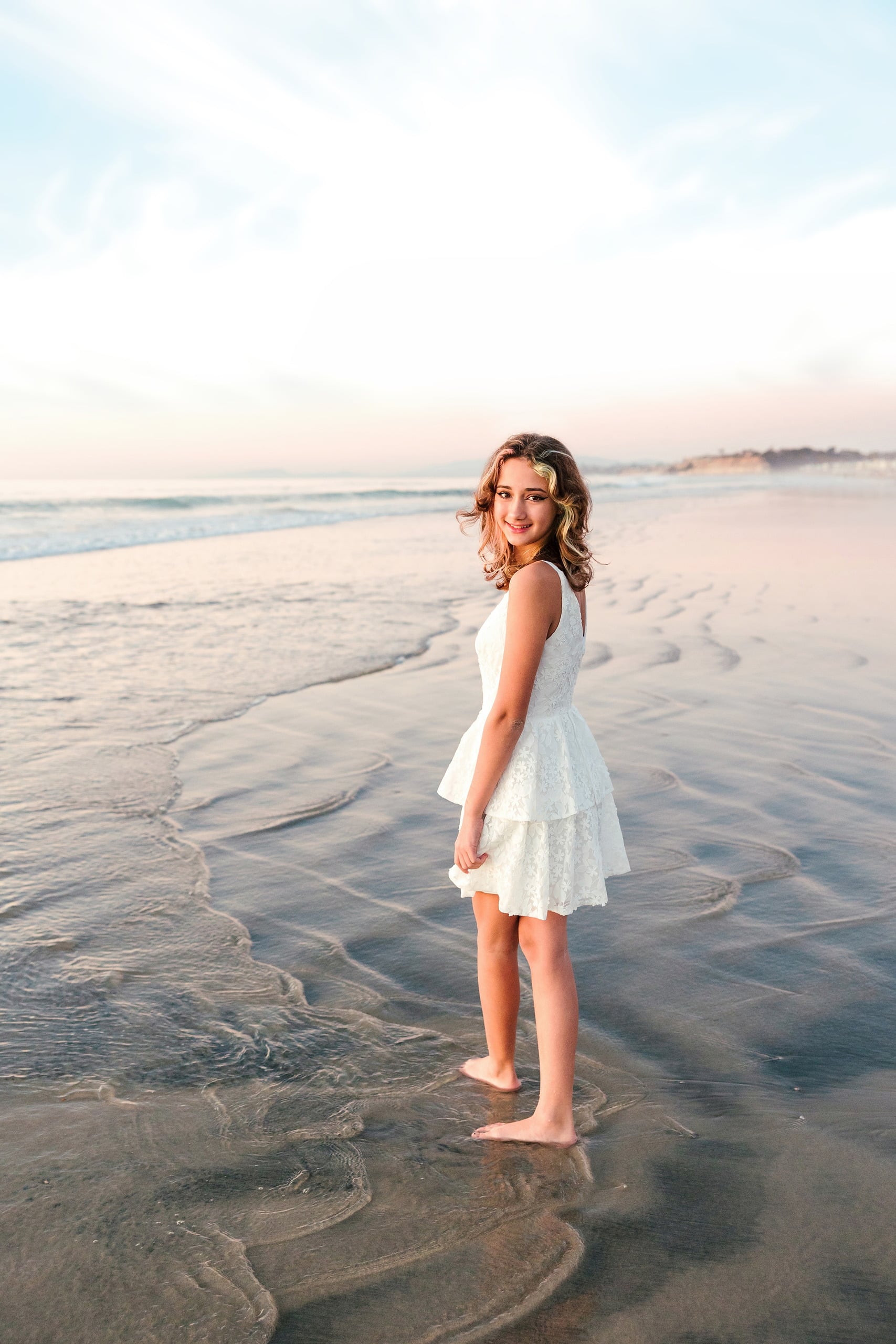 The Day the Sun Stood Still — 16 Teen in white dress standing on wet beach sand looking back at golden hour