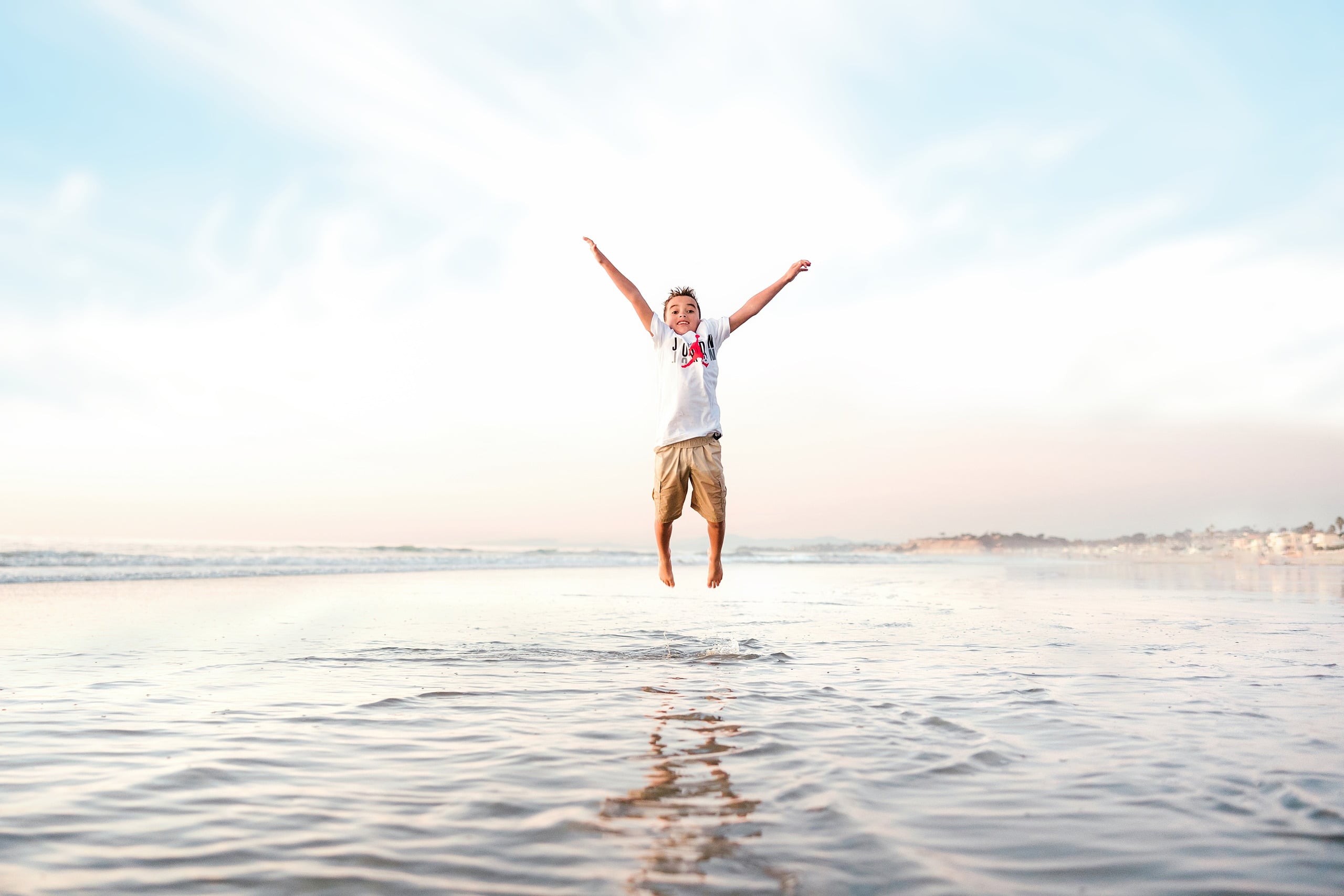 The Day the Sun Stood Still — 18 Child jumping with arms raised high on wet beach sand at sunset at Del Mar