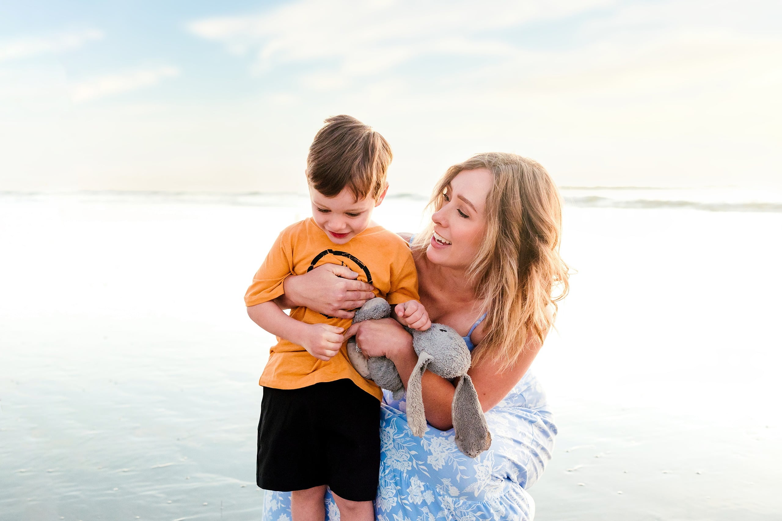 The Day the Sun Stood Still — 34 Woman holding and smiling down at toddler on wet beach sand at sunset