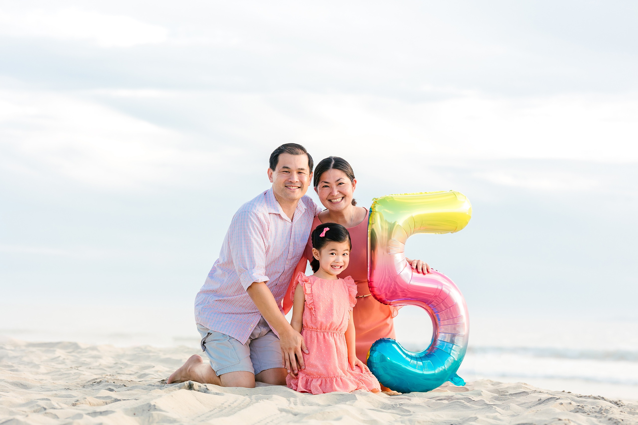 Turning Five on Coronado — 02 Ava with mom and dad holding a large number five balloon on sandy Coronado beach