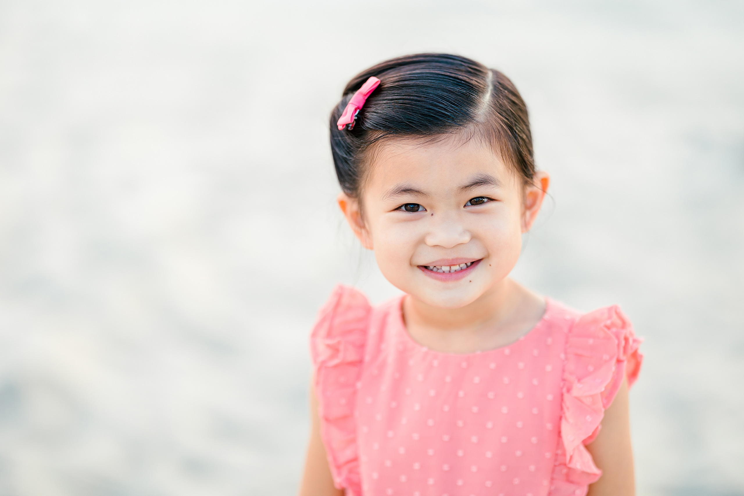 Turning Five on Coronado — 07 Ava in ruffled pink dress smiling against blurred beach background