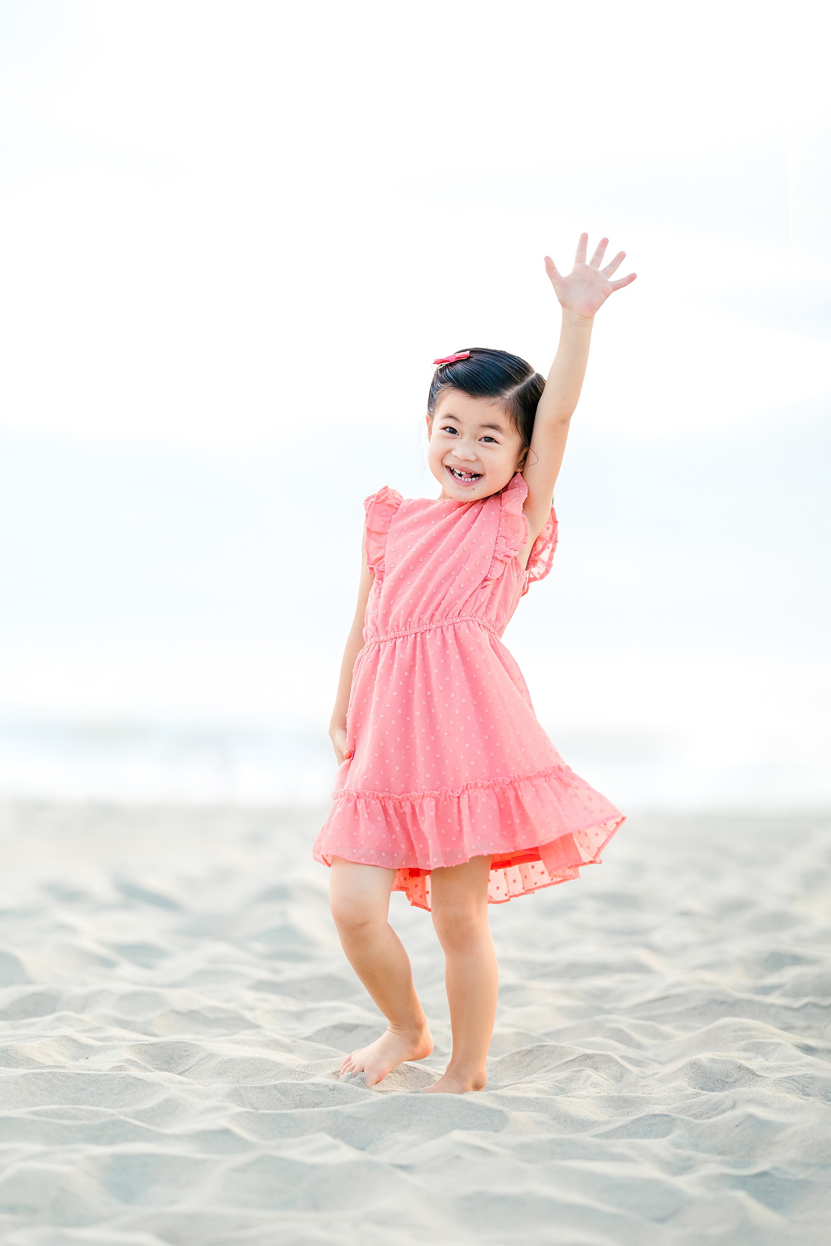 Turning Five on Coronado — 08 Ava standing with arm raised in celebration on the sandy beach shore