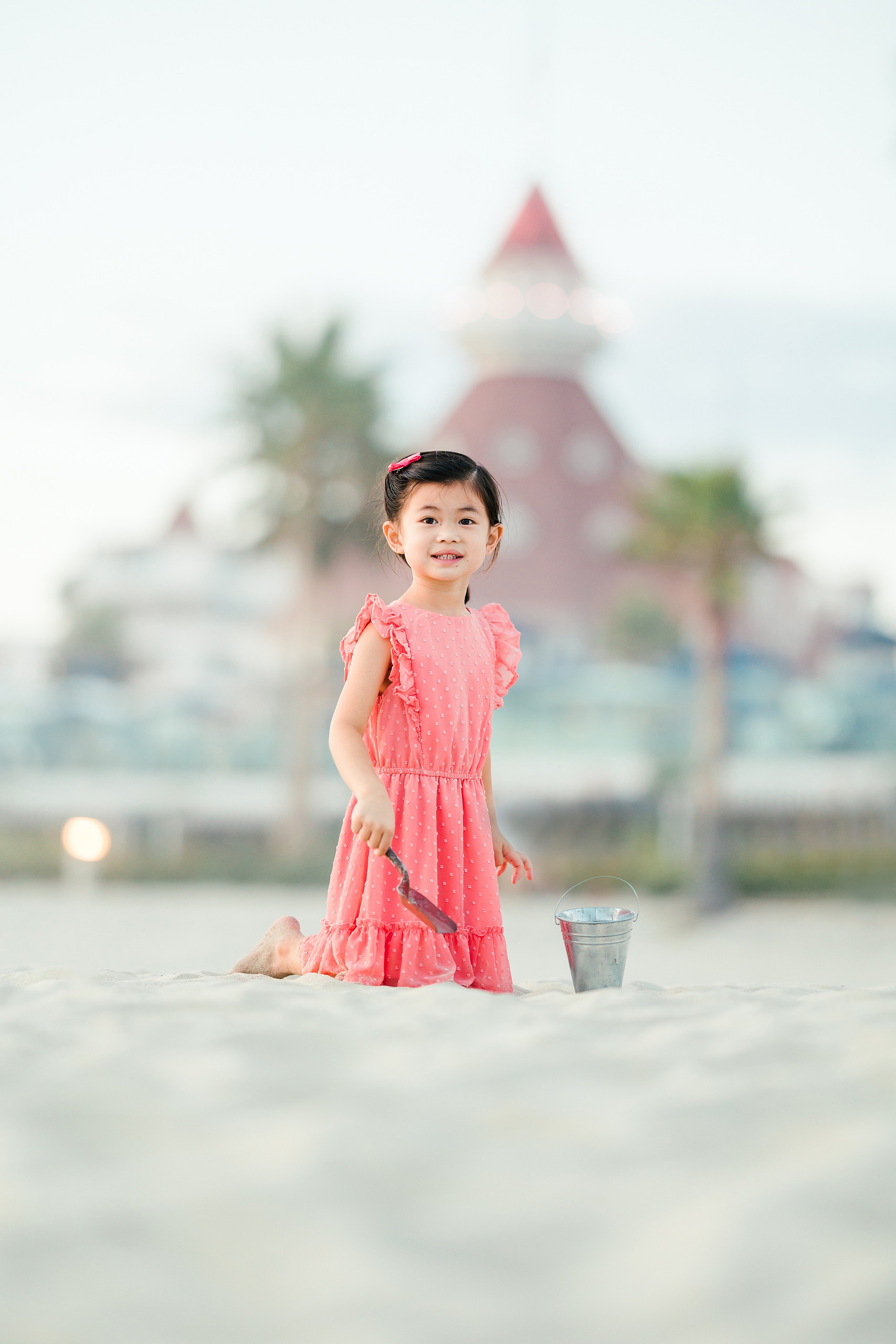 Turning Five on Coronado — 33 Ava kneeling on sand near Hotel del Coronado tower blurred in background