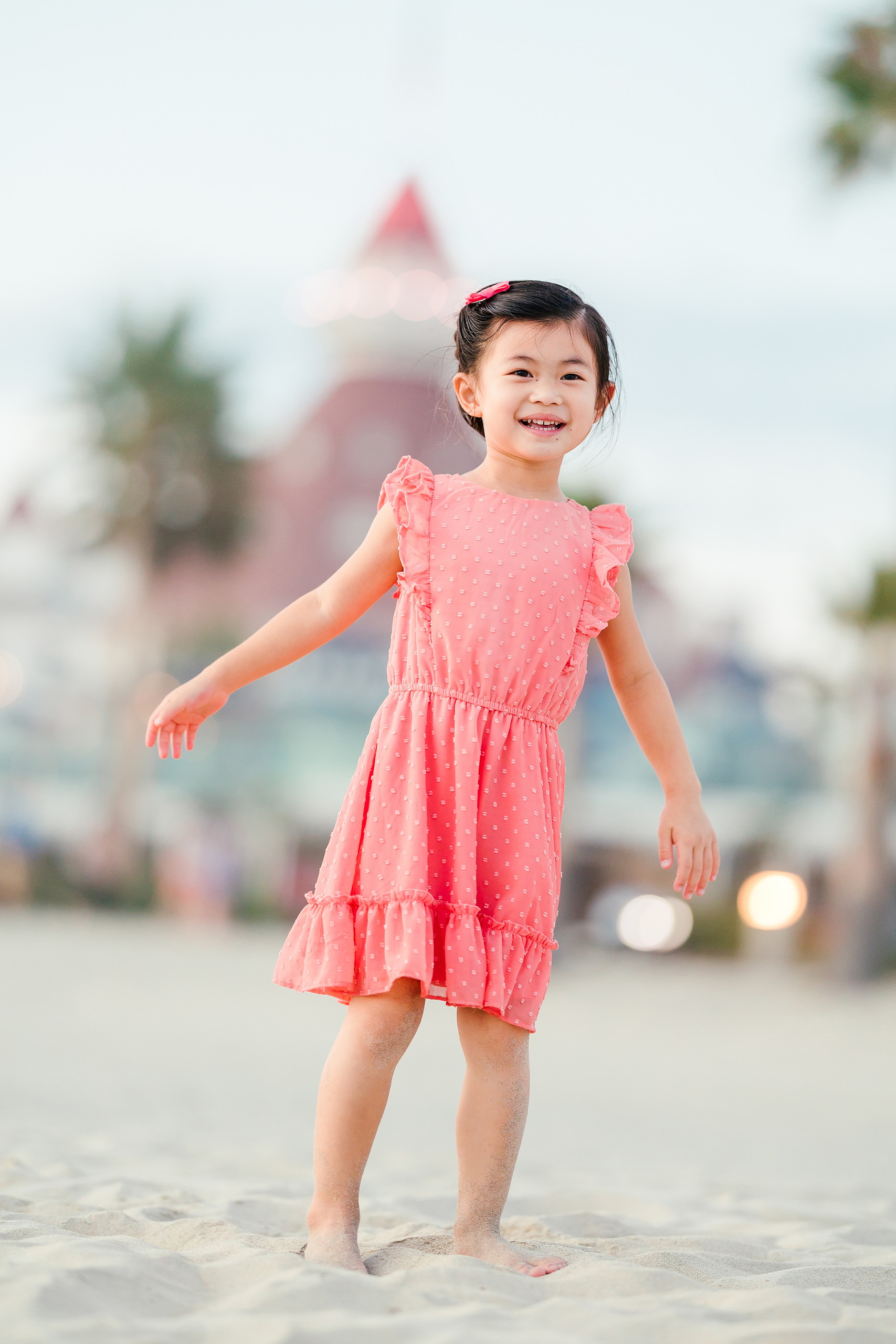 Turning Five on Coronado — 35 Ava standing on beach with arm extended, Hotel del Coronado tower soft focus