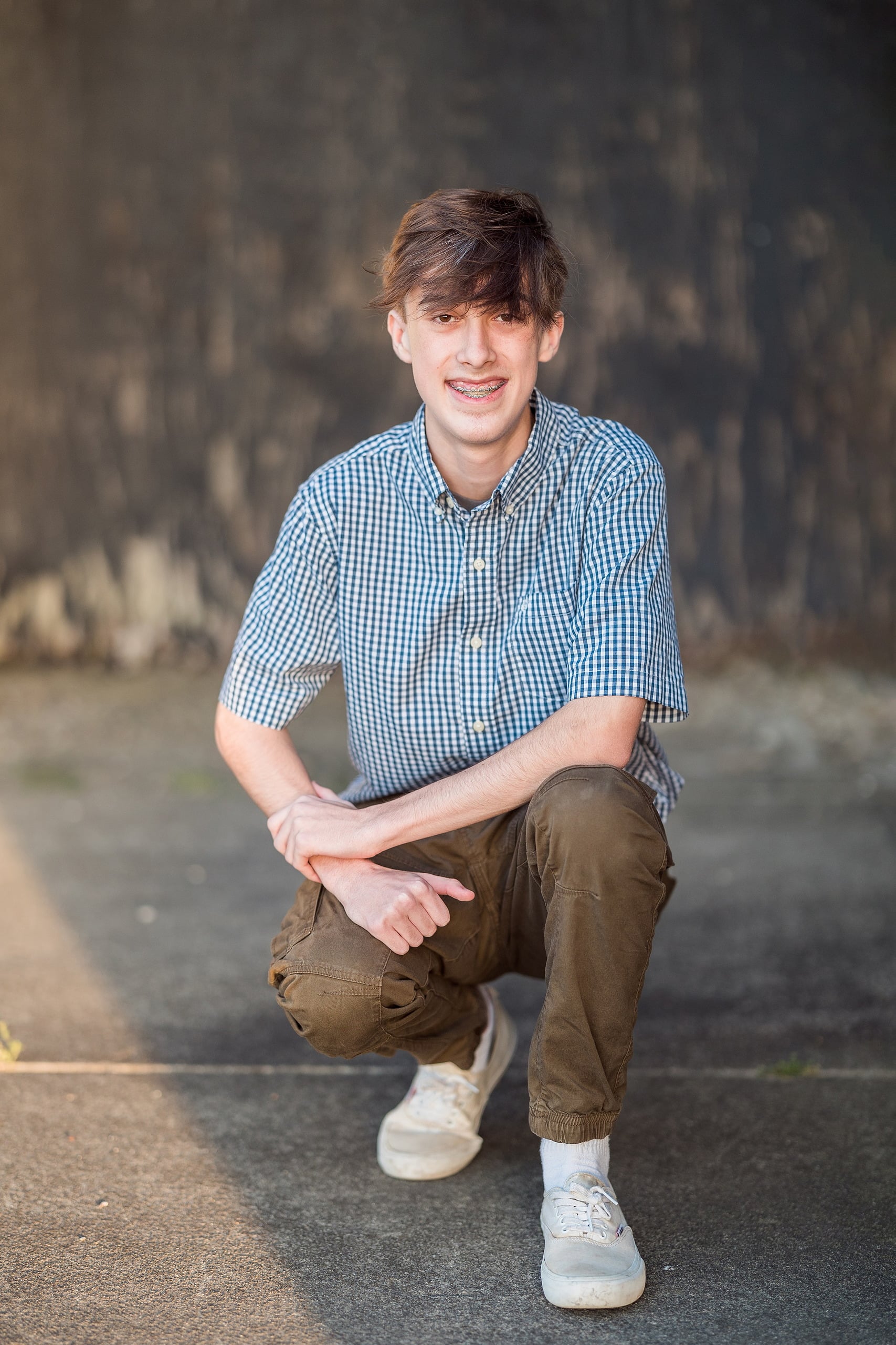 Zach’s Senior Portraits — 01 Zach crouching and smiling against weathered concrete at Fort Monroe, Hampton