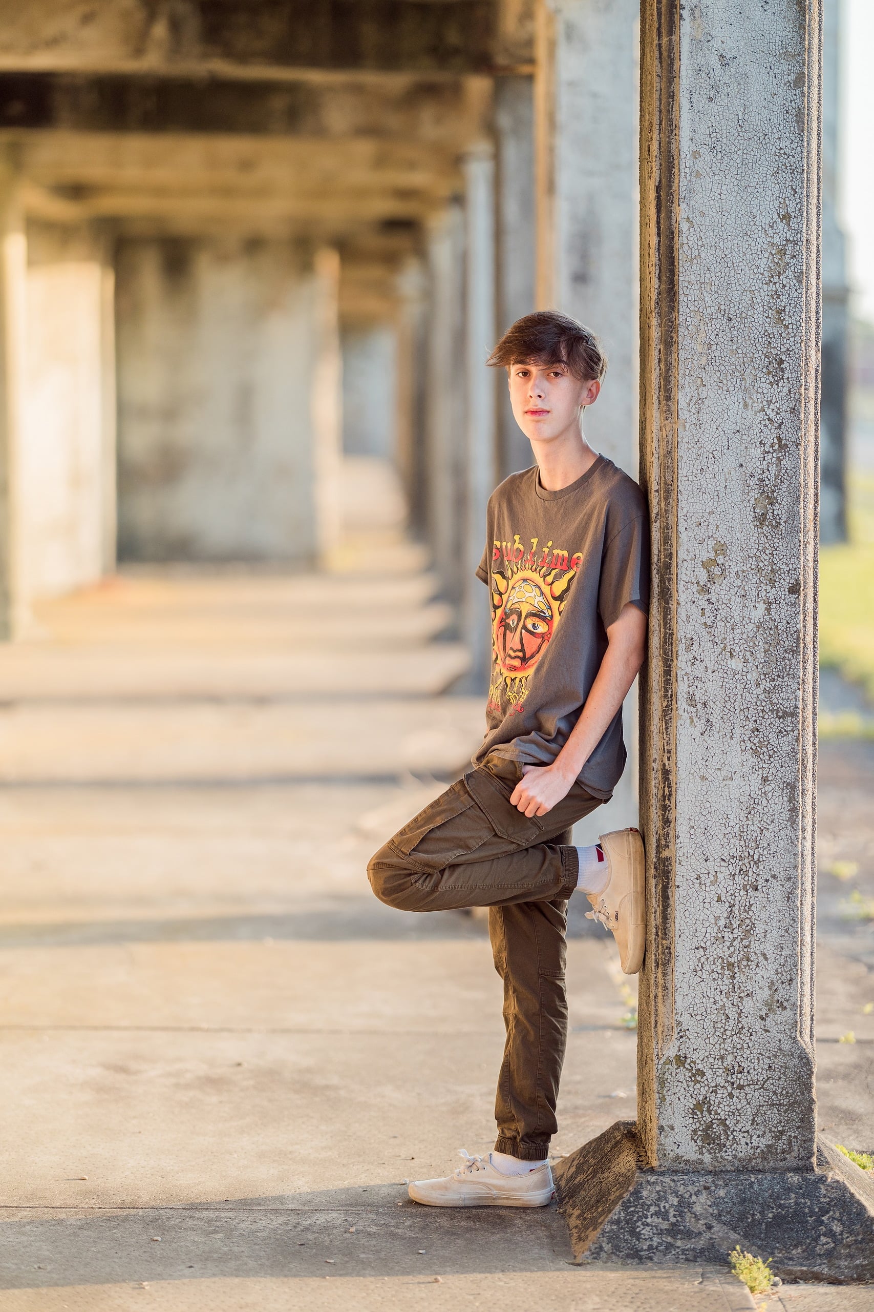 Zach’s Senior Portraits — 04 Zach standing with leg raised against industrial pillar at Fort Monroe