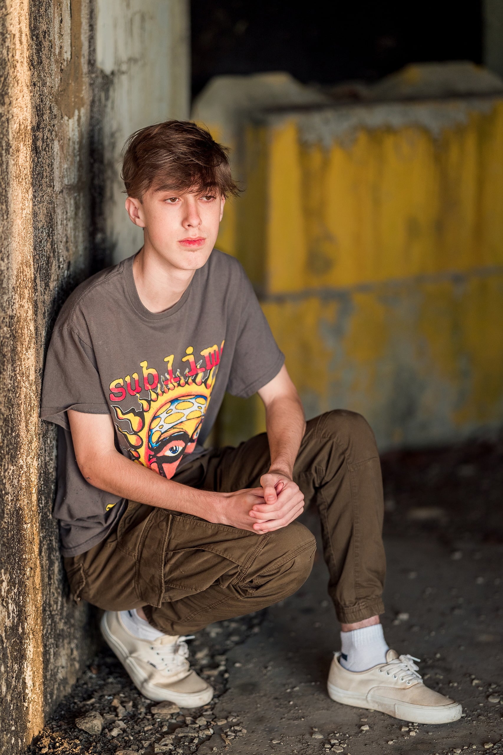 Zach’s Senior Portraits — 08 Zach crouching against weathered pillar, thoughtful pose at Fort Monroe