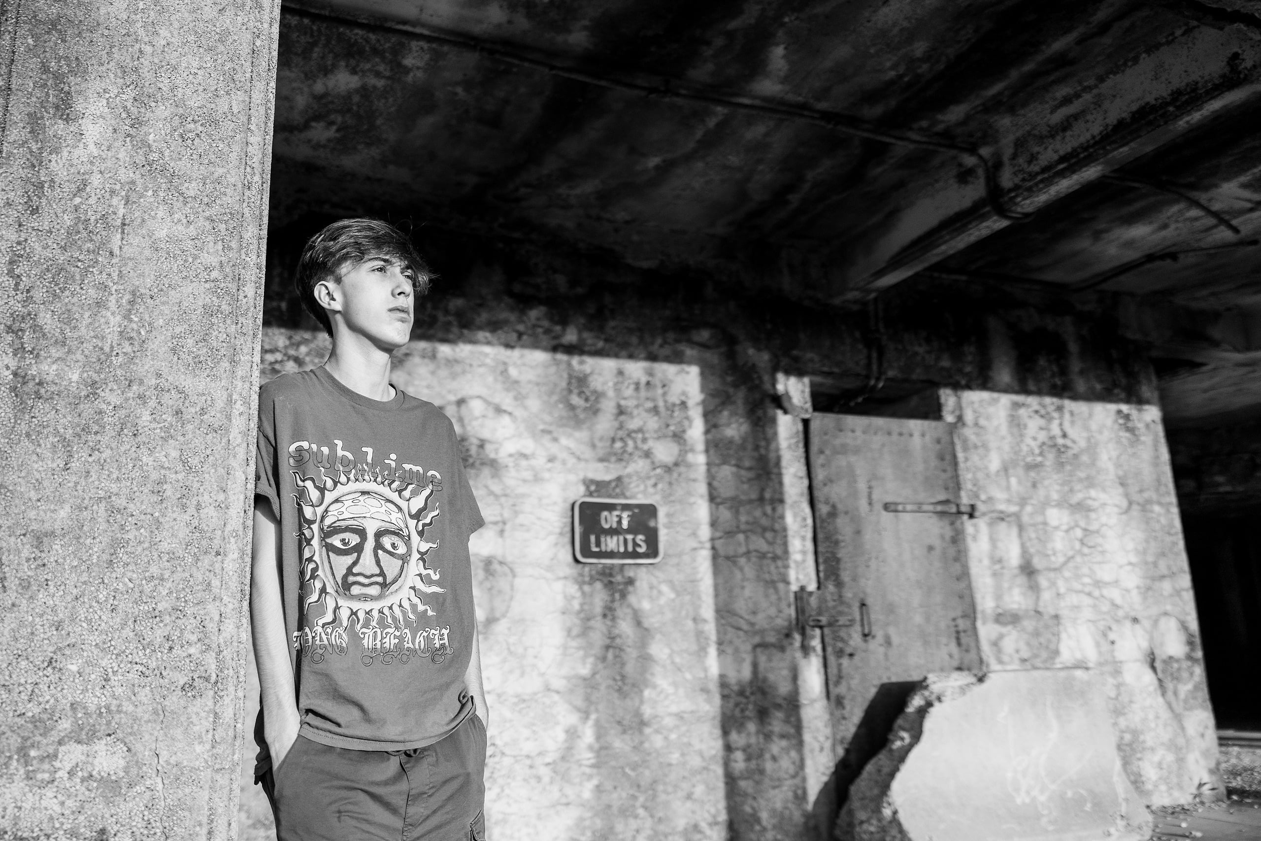 Zach’s Senior Portraits — 11 Zach looking upward in industrial passage, black and white, Off Limits sign