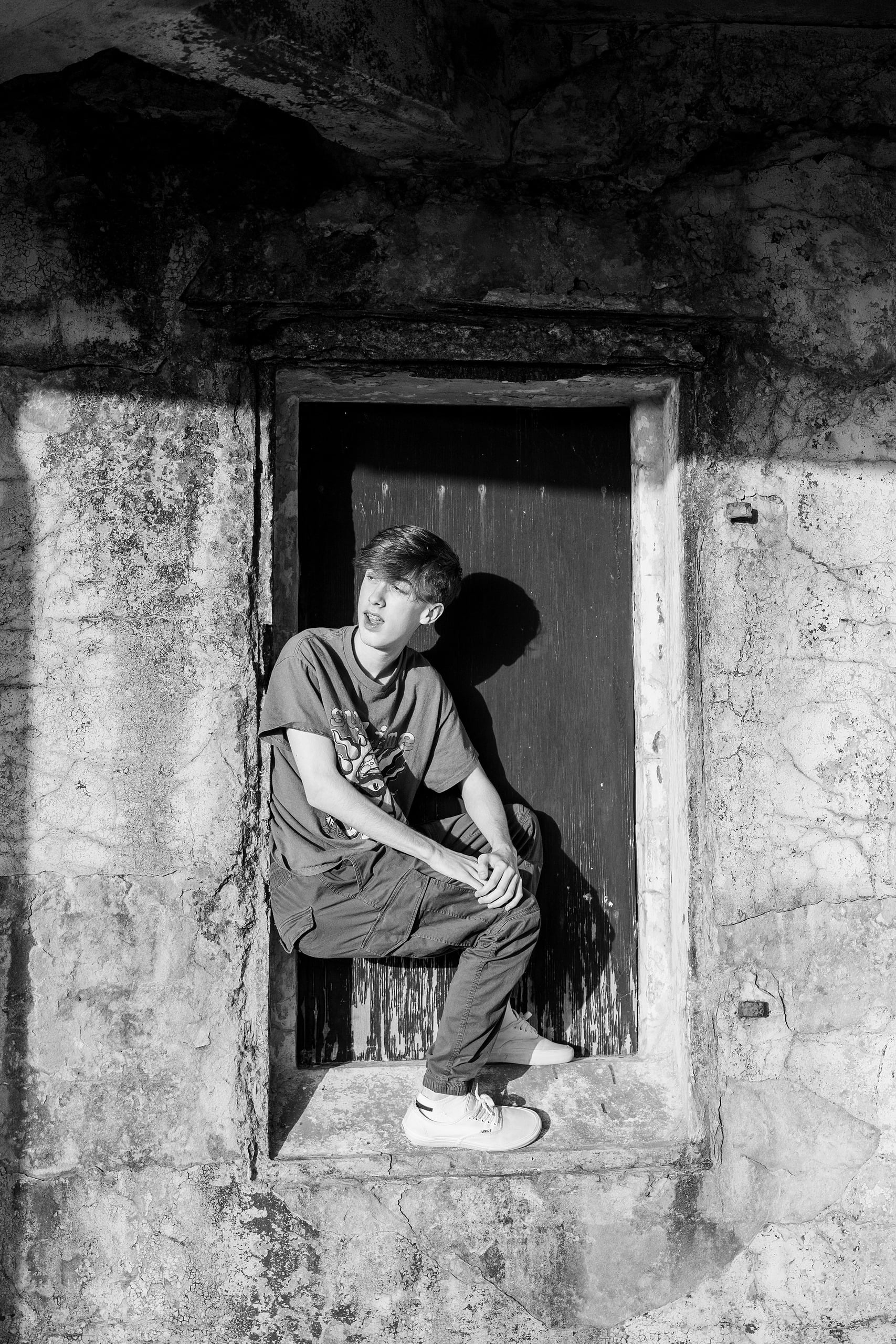 Zach’s Senior Portraits — 14 Black and white: Zach crouched in doorway at Fort Monroe Battery