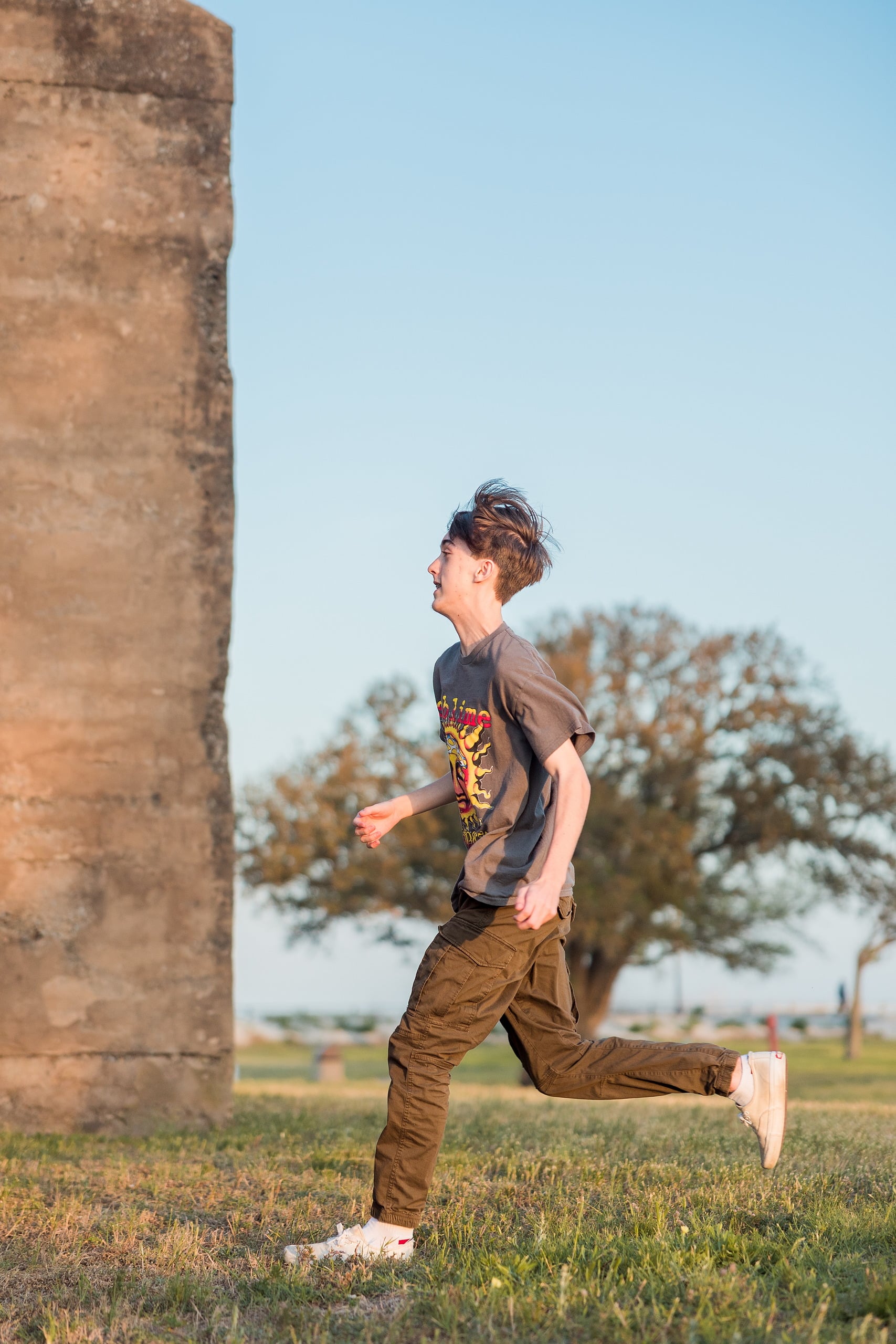 Zach’s Senior Portraits — 15 Zach running past weathered brick battery structure in open field