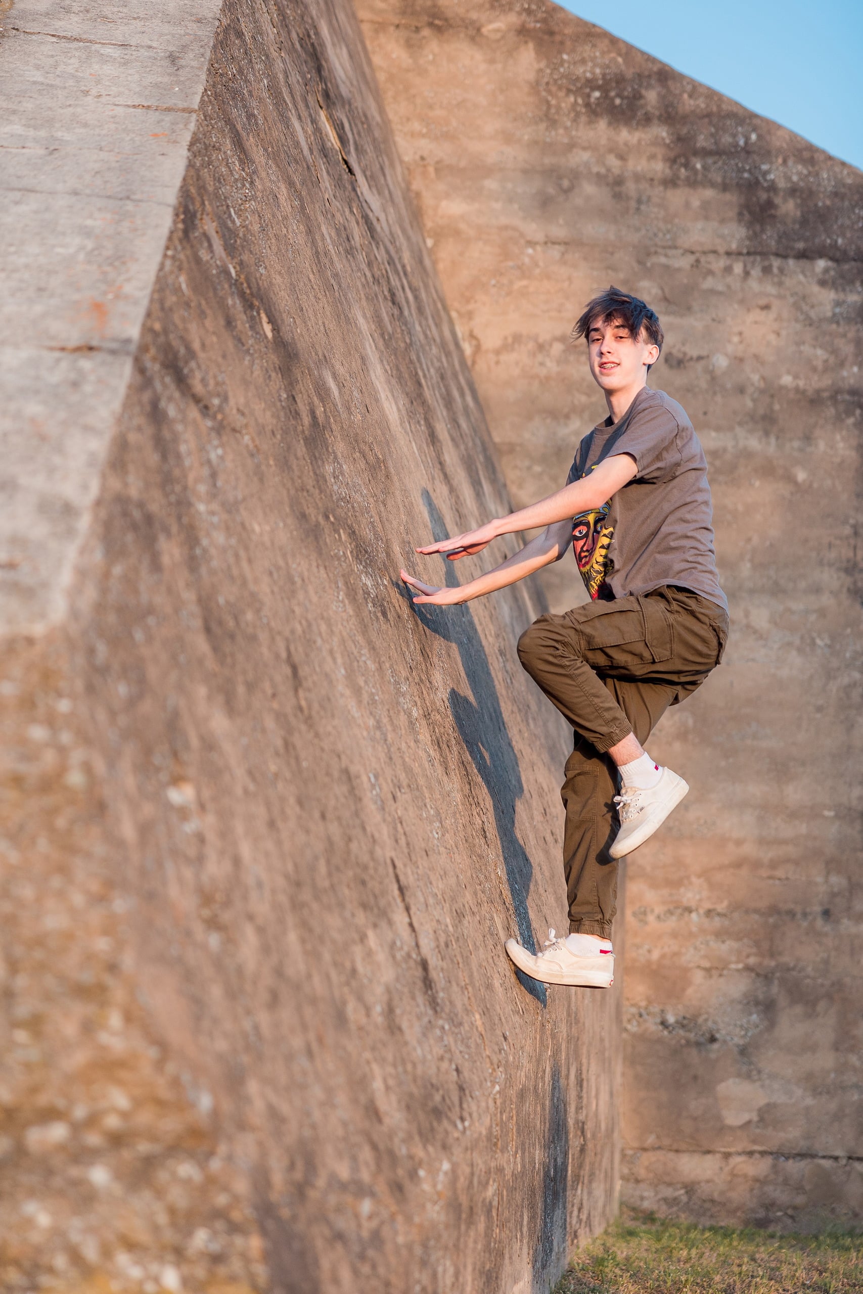Zach’s Senior Portraits — 17 Zach climbing brick wall with arms outstretched, playful pose