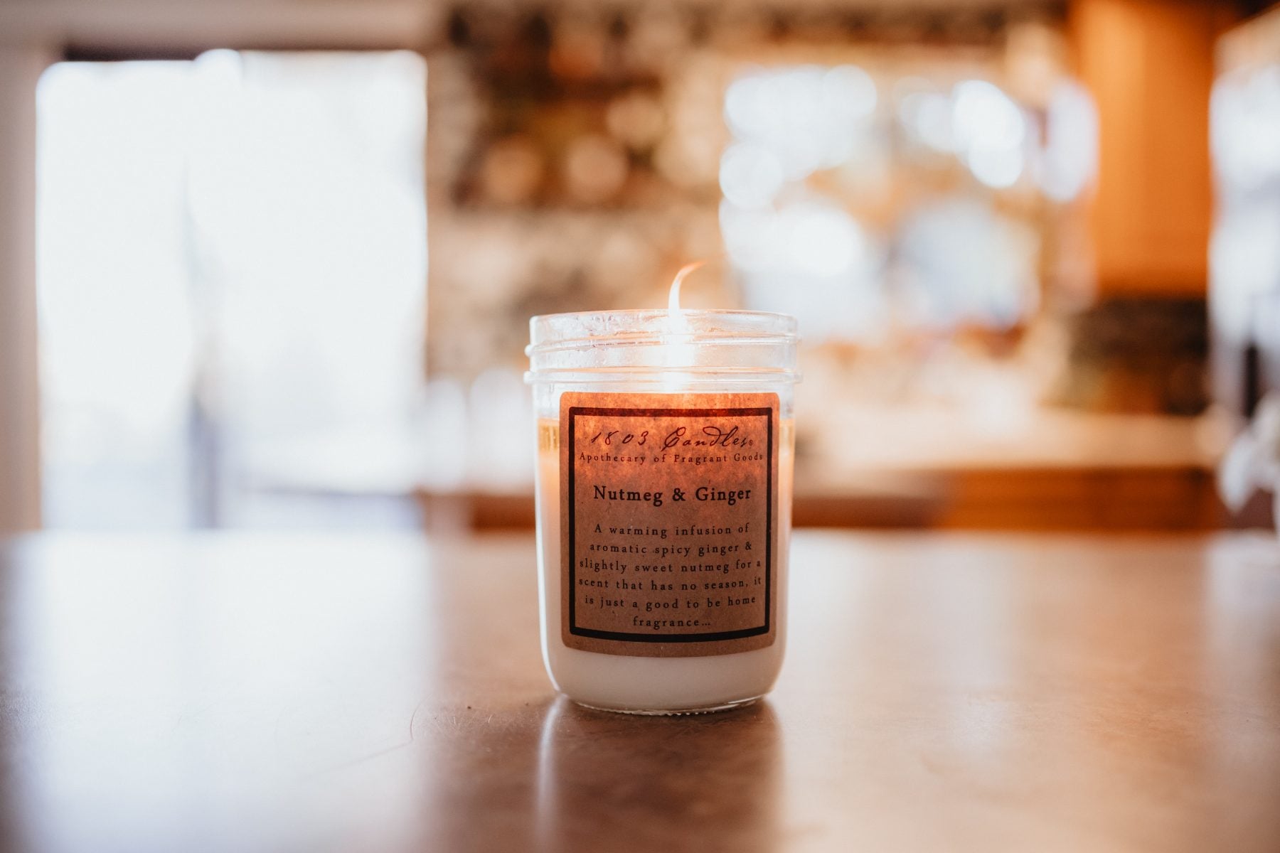 Lit candle labeled Barnyard and Ginger glows on a wooden table