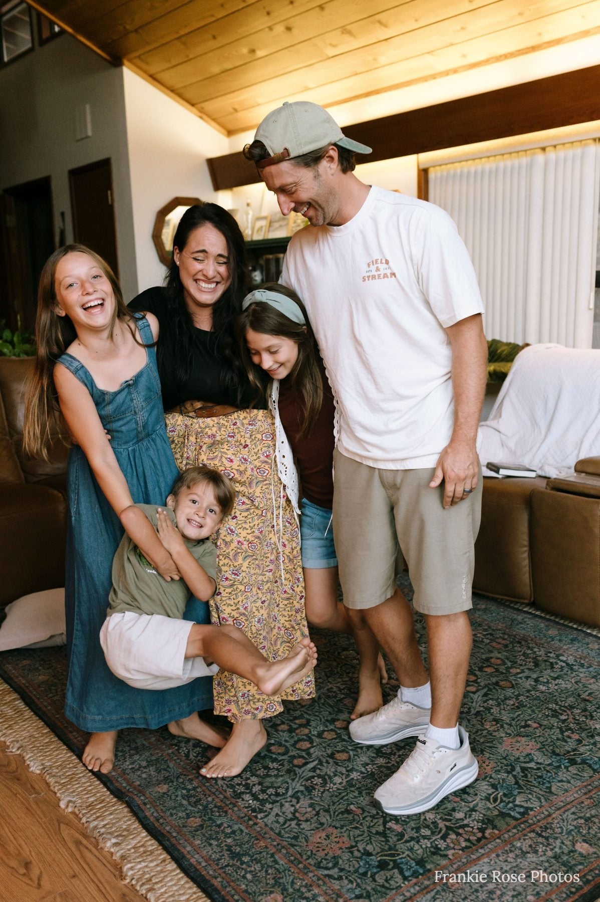 Mom and dad laugh with three kids, one held upside down by leg