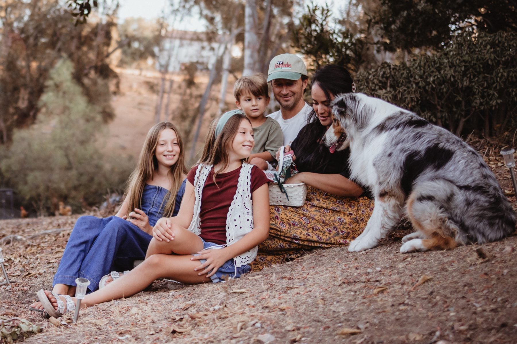 Family of five sits on fallen leaves with dog in Lakeside, San Diego family photographer session