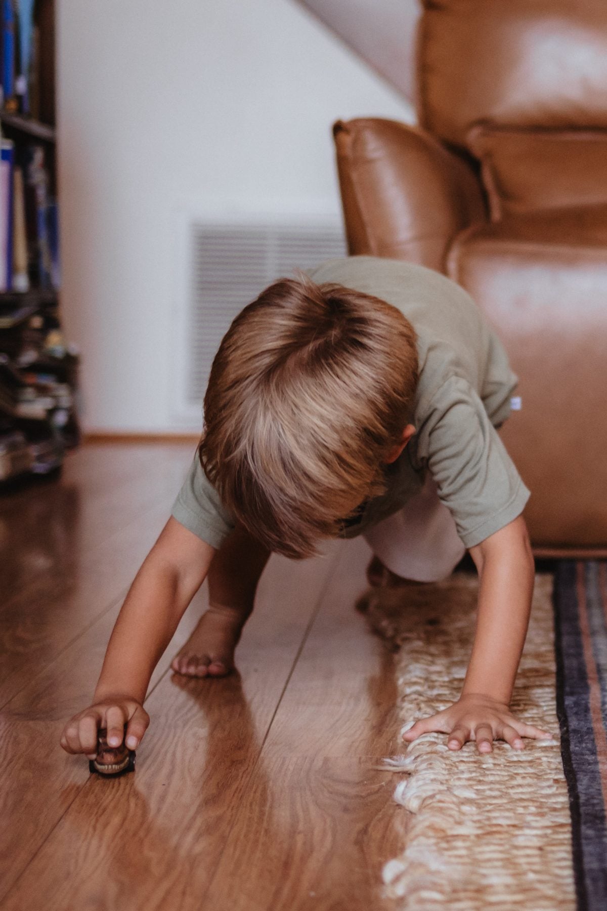 Barefoot boy crawls on wood floor chasing a toy car in Lakeside