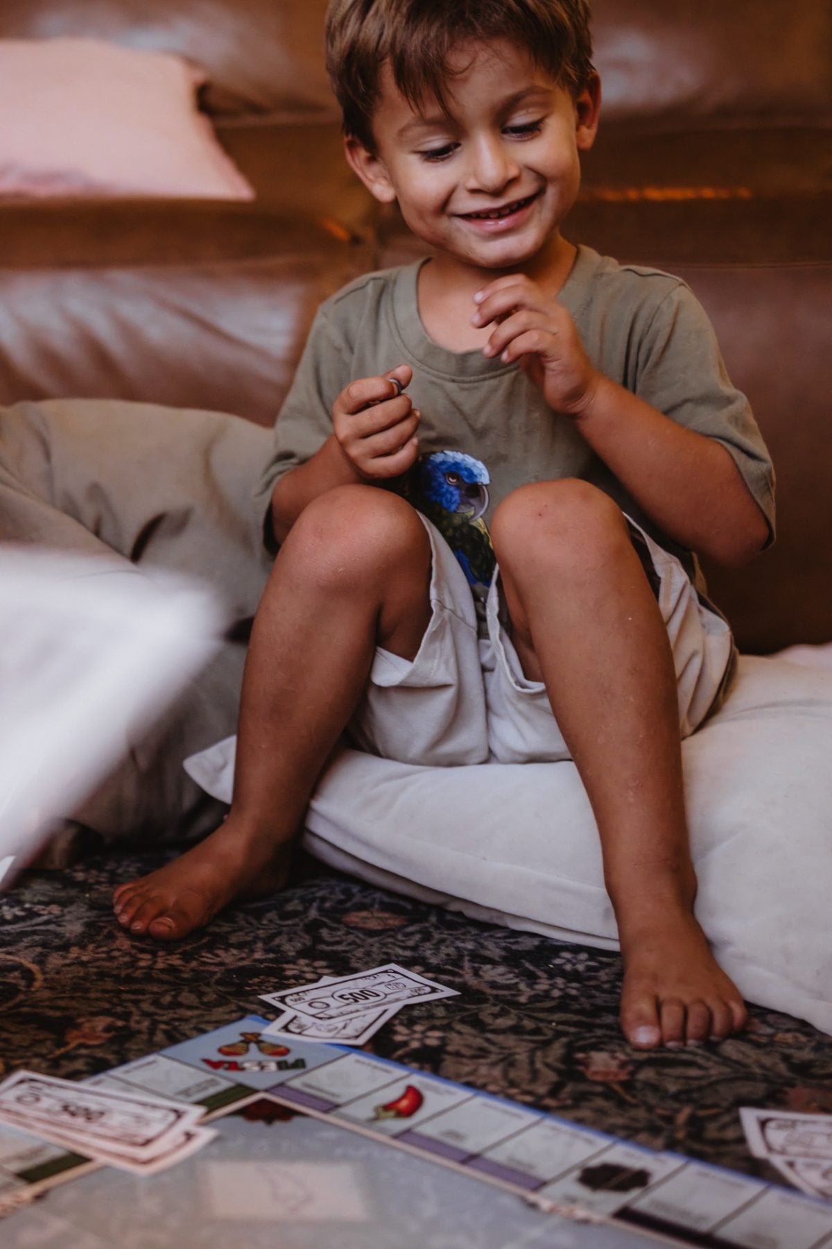 Barefoot boy smiles while playing a board game on a pillow