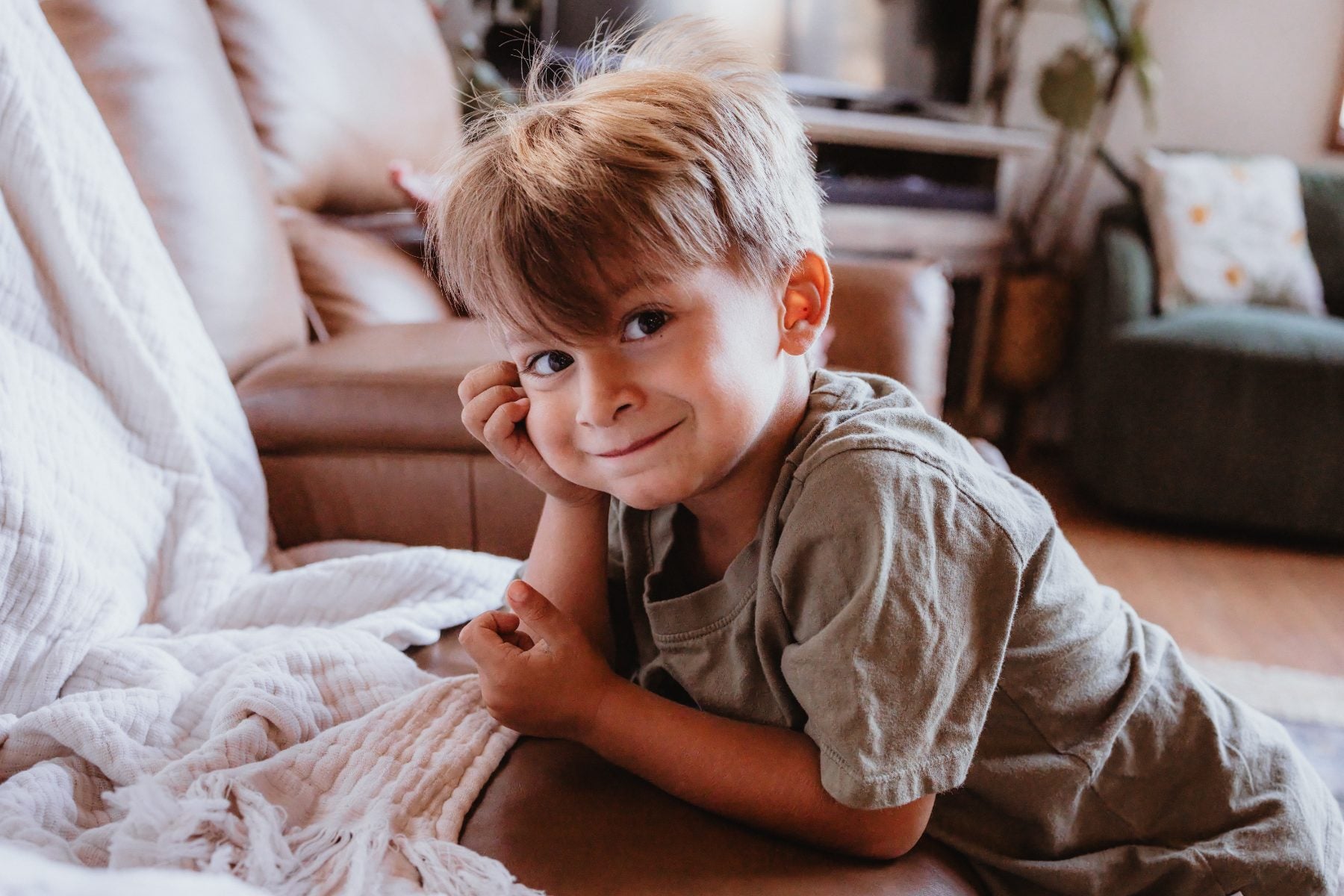 Boy rests chin on hand, smiling playfully on living room couch