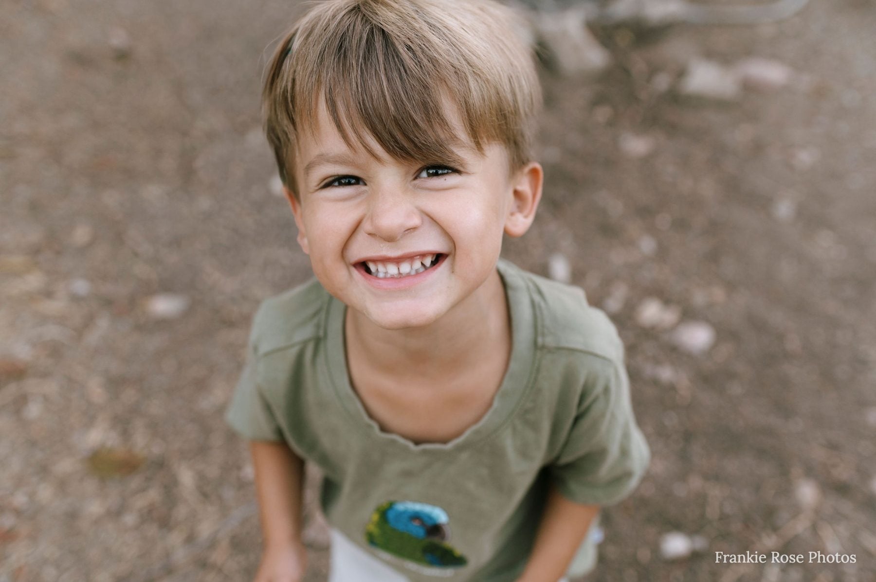 Wide, cheerful smile from a young boy on a gravel path