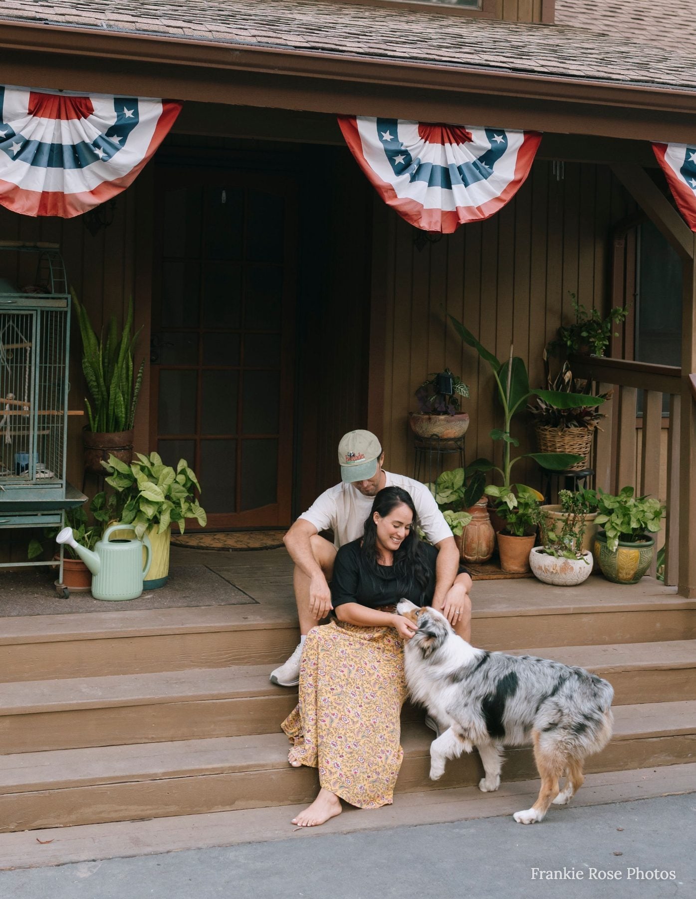 Couple petting Australian shepherd dog on porch with patriotic banners
