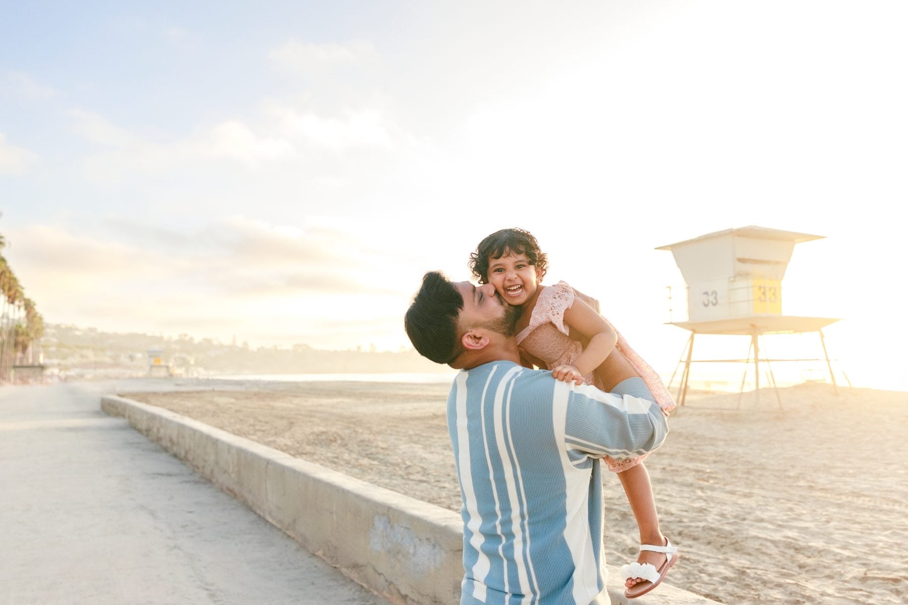 Dad lifts giggling daughter onto his shoulders near lifeguard tower, La Jolla Shores