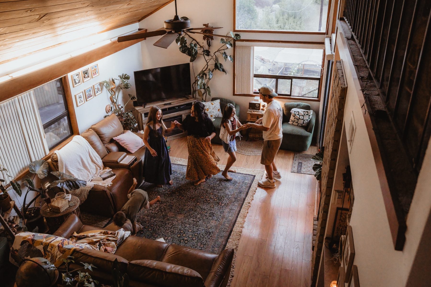 Family dances together in sunlit Lakeside living room, aerial view