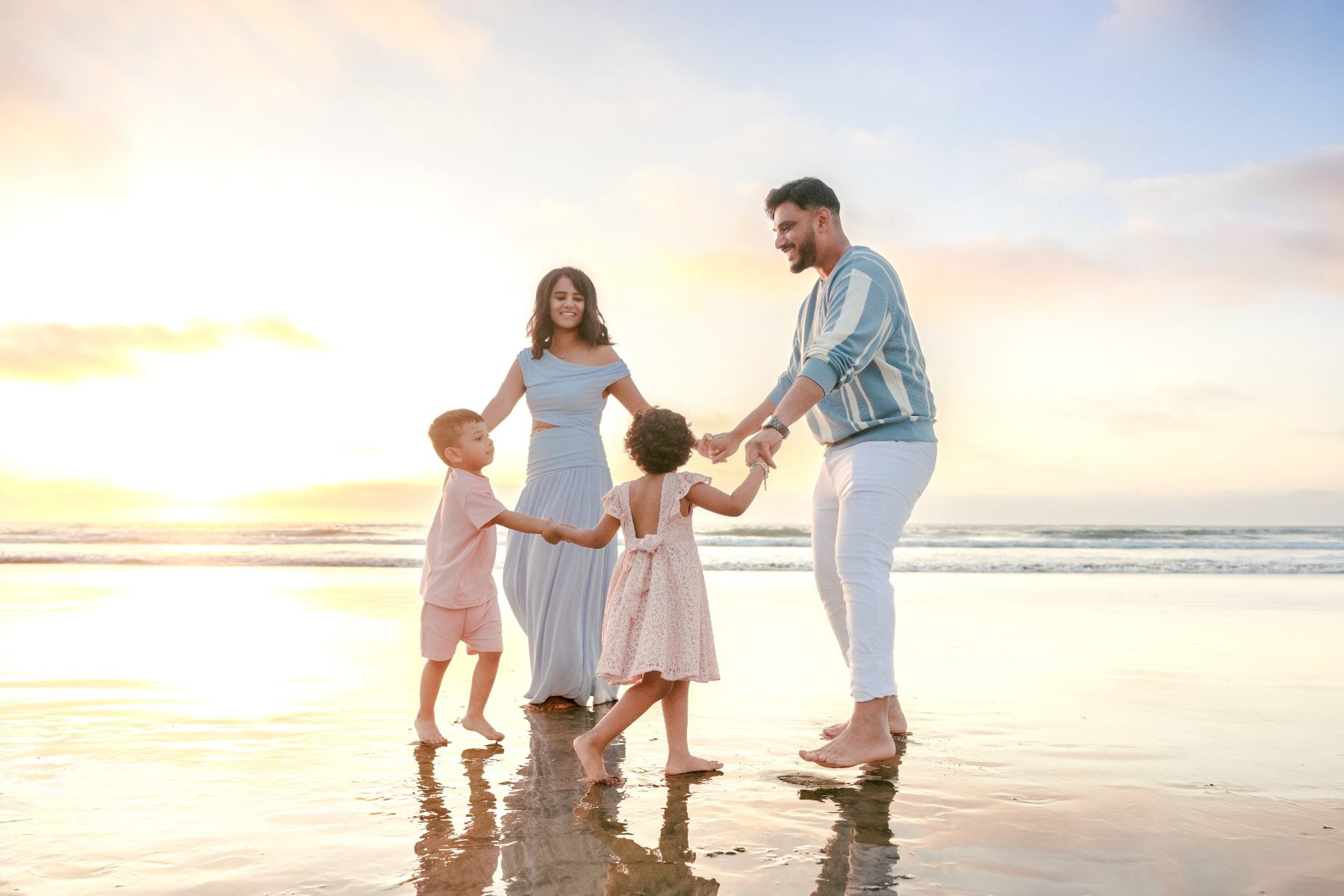 Family of four joins hands dancing on sand at sunset