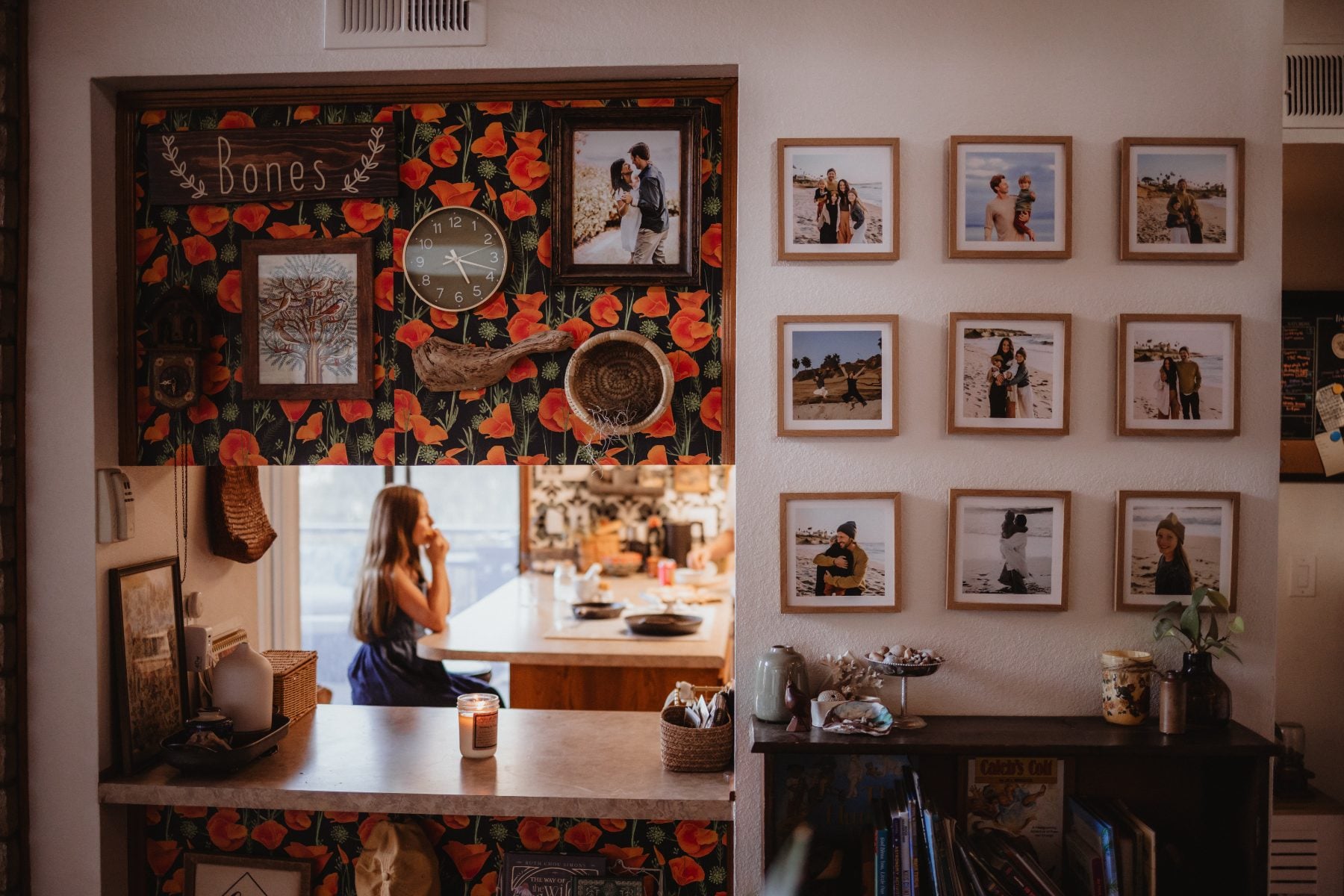 Gallery wall of family photos with woman visible through kitchen pass-through