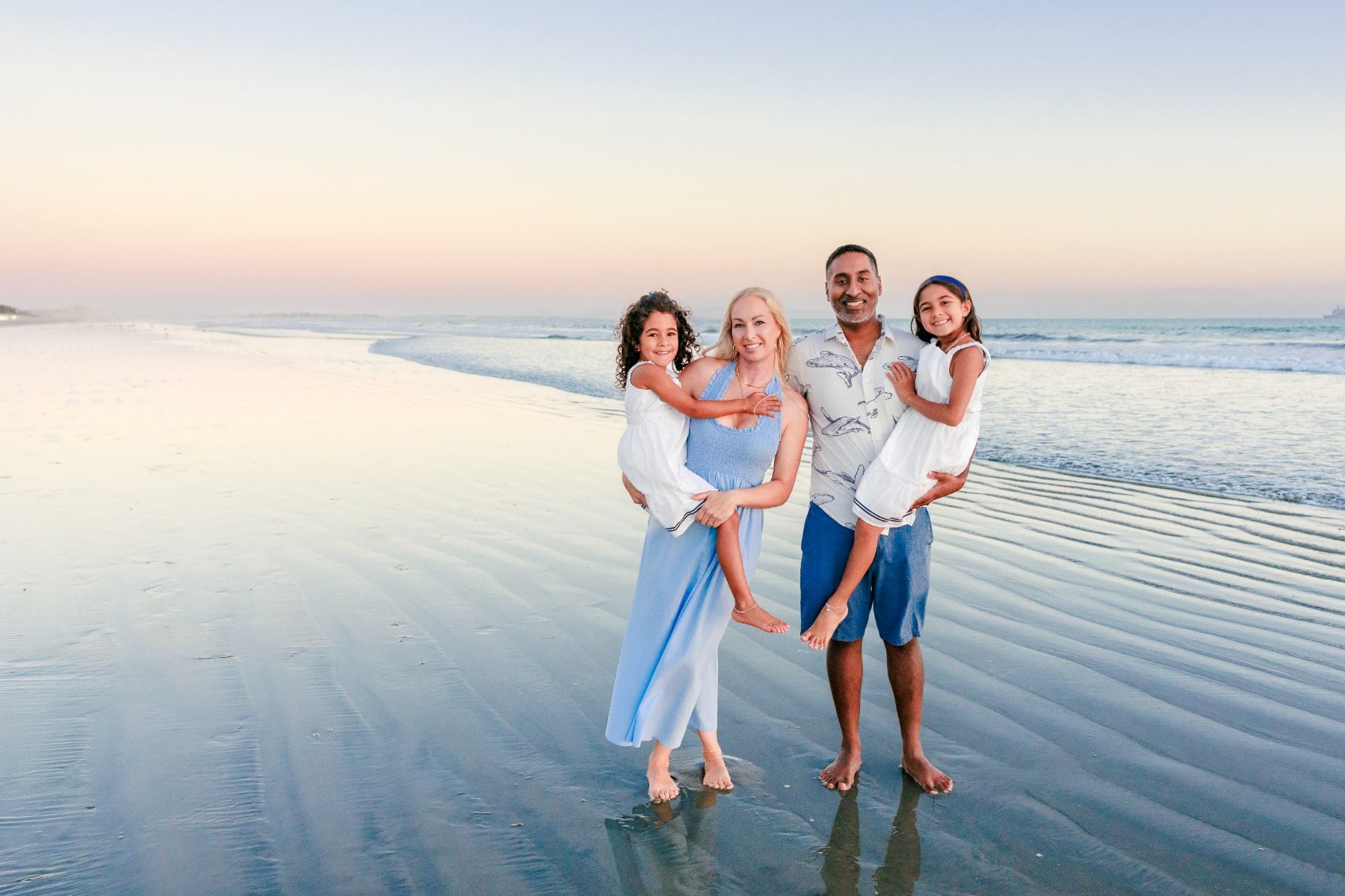 Parents hold their daughters while smiling together on Coronado Beach