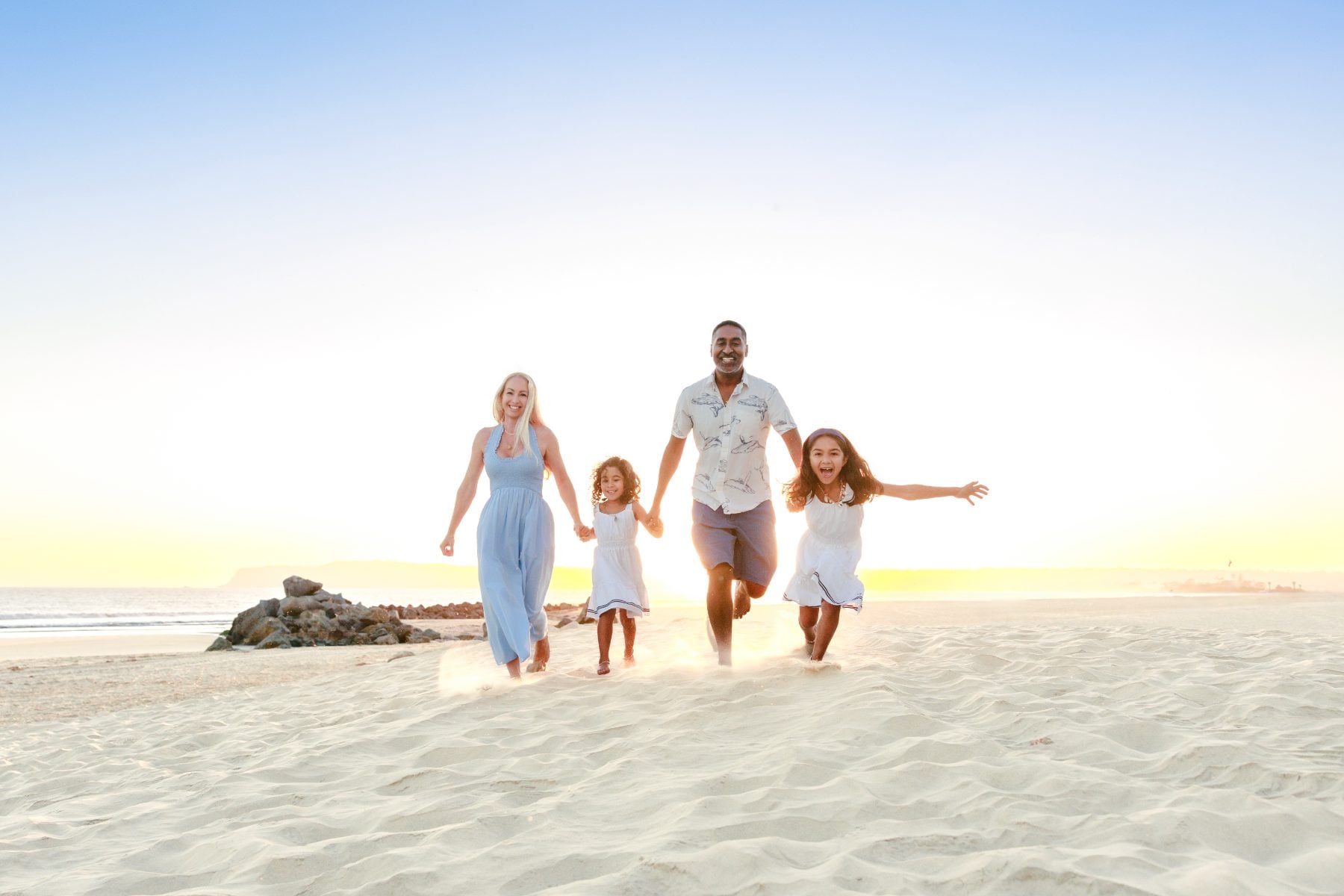 Family of four runs laughing across the sand for beach family photos San Diego