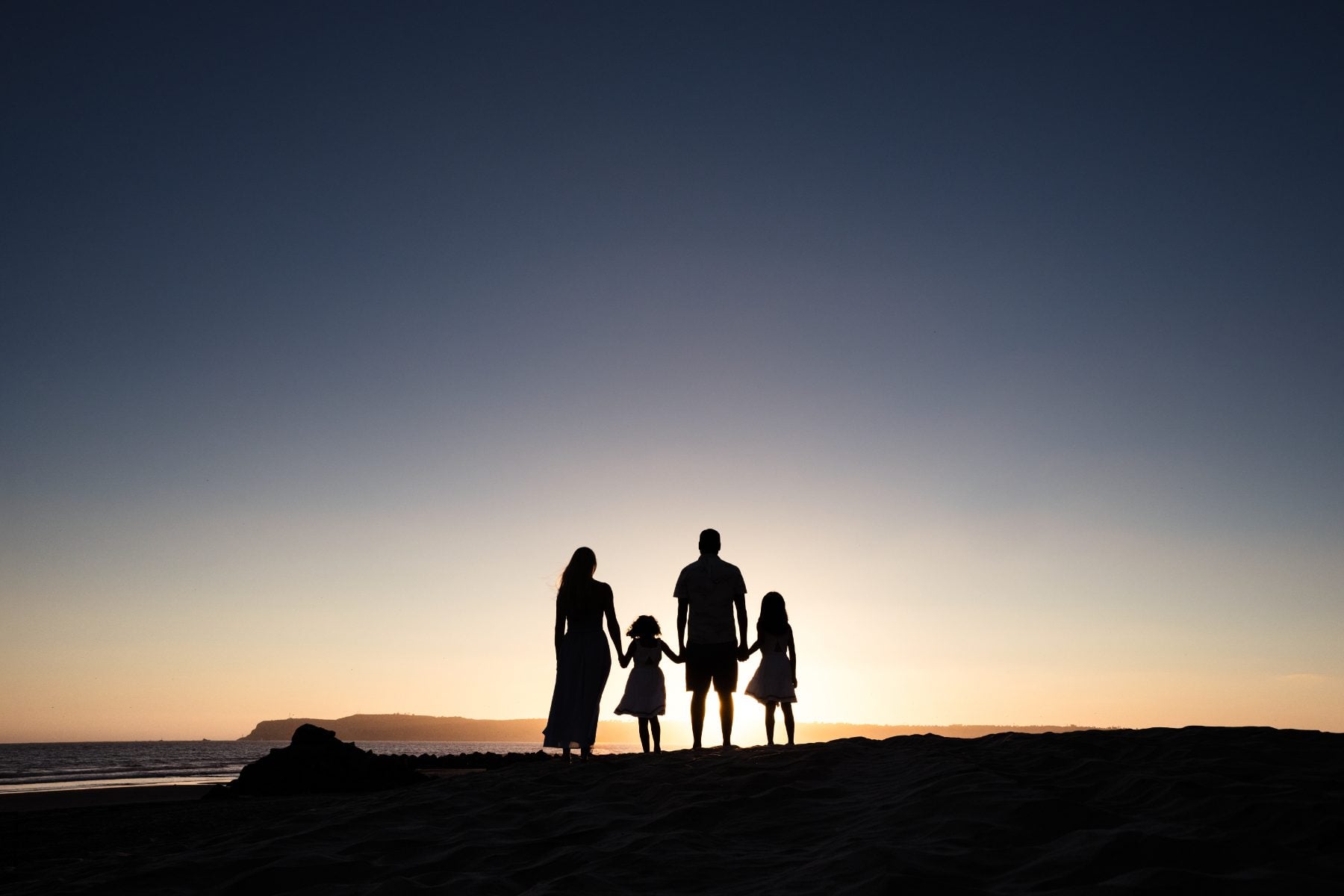 Family of four stands in silhouette watching the sunset at Coronado Beach
