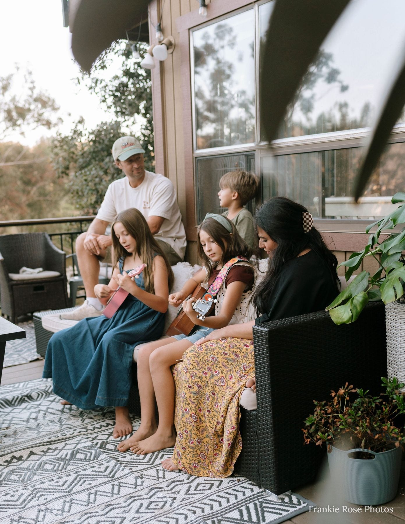 Family of five plays ukuleles together on a cozy patio rug